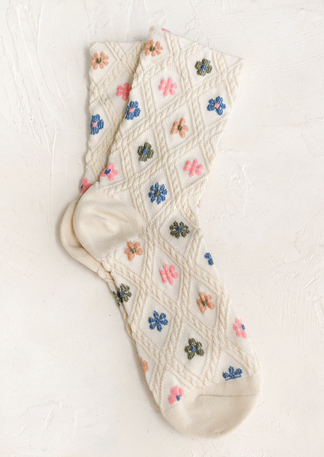 A pair of cream socks with pink, tan green and blue flowers.