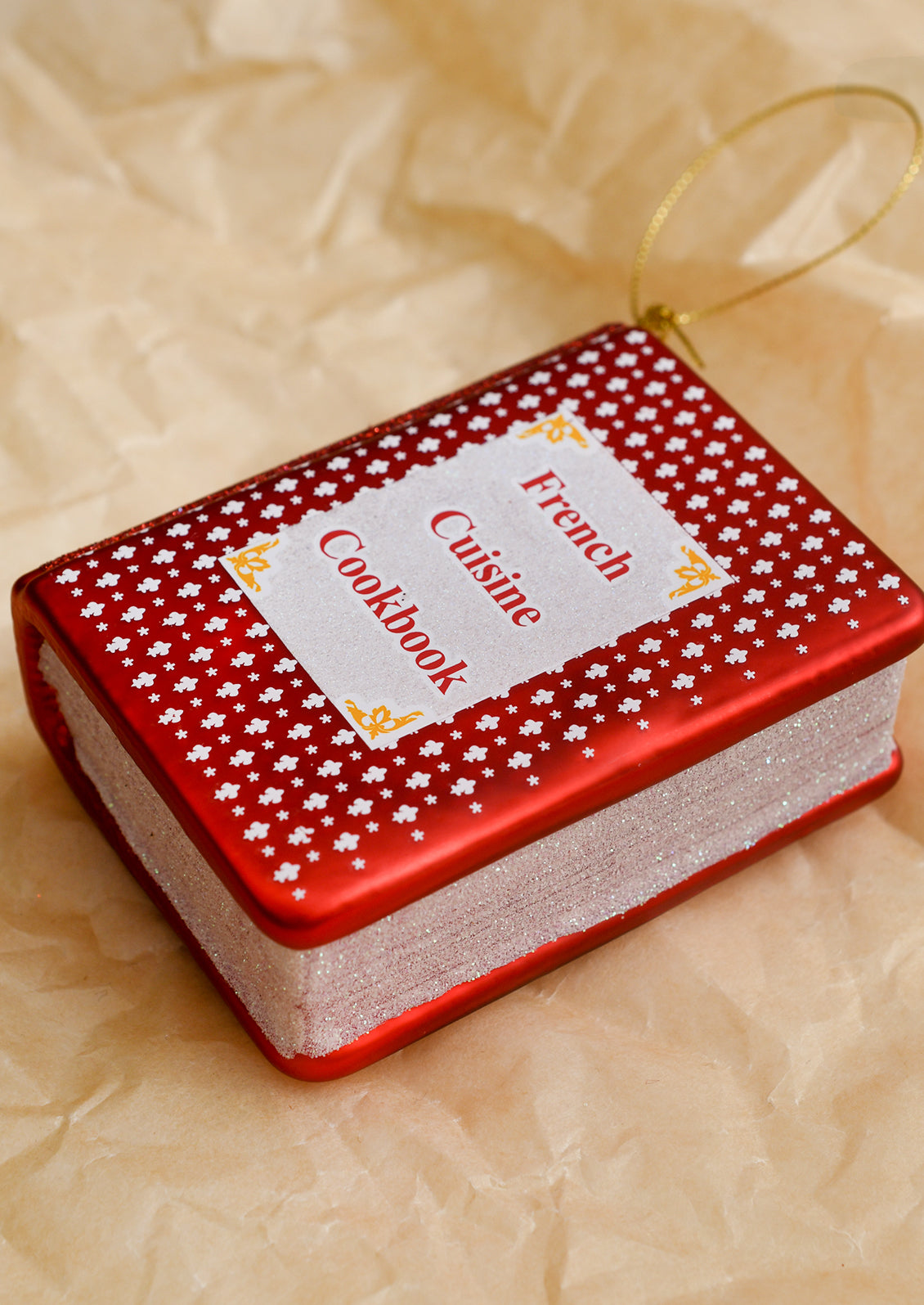 A glass ornament of a red cookbook reading "French Cuisine Cookbook" on cover.