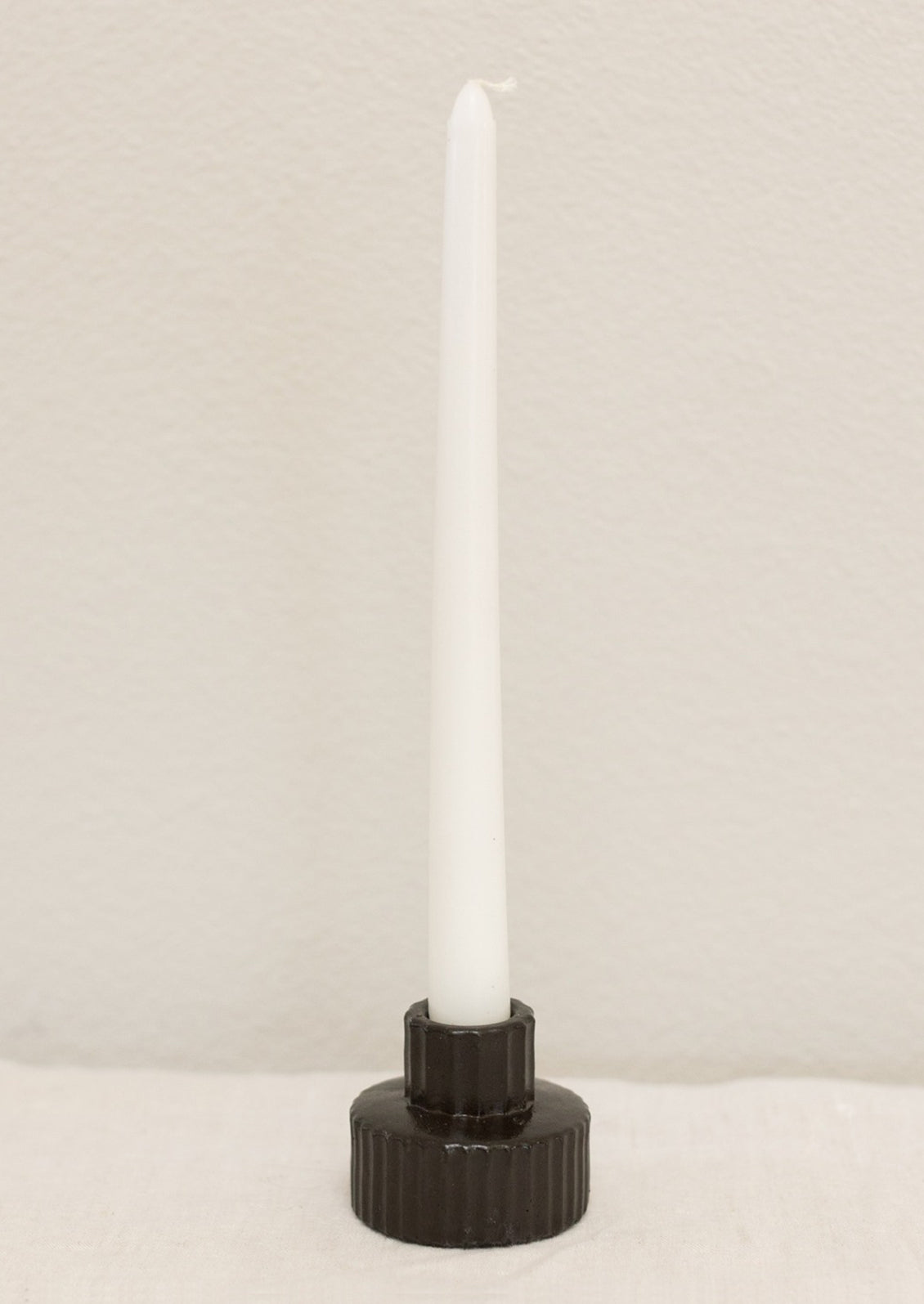 A short and wide fluted concrete taper candle holder in charcoal.