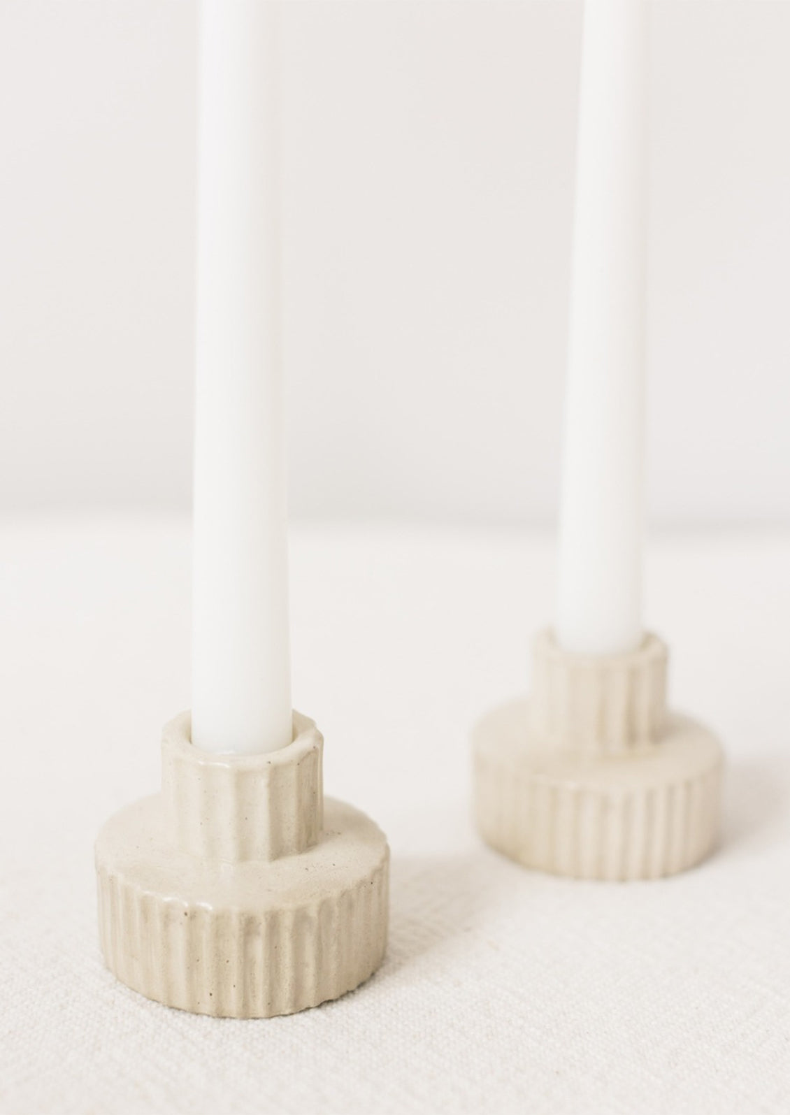 A short and wide fluted concrete taper candle holder in natural.
