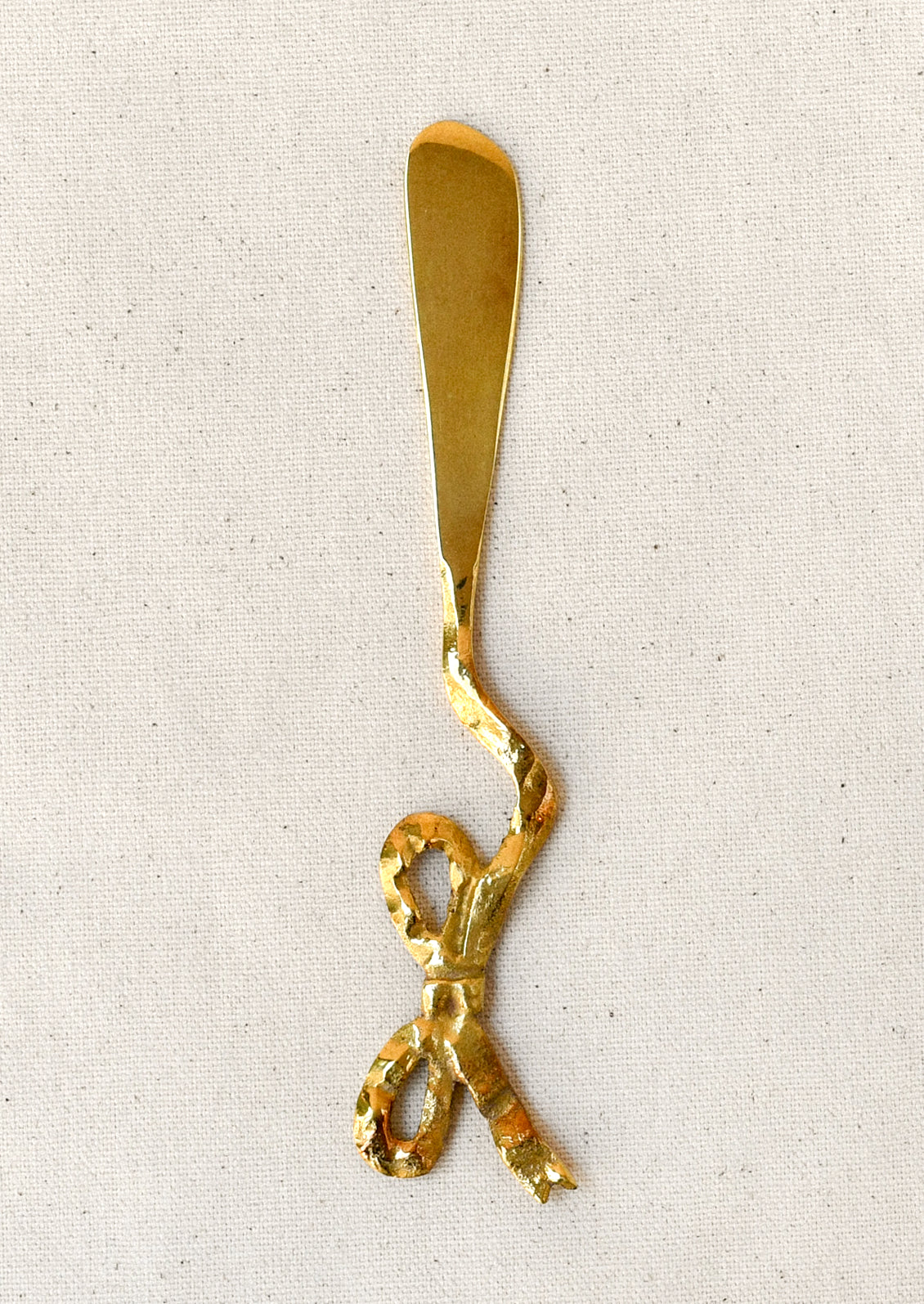 A brass spreader knife with a bow shaped design.