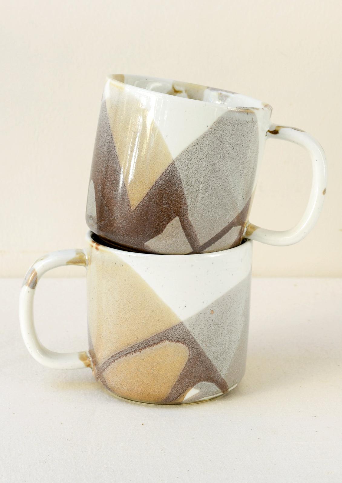 A white ceramic mug with a painted abstract design in brown and grey.