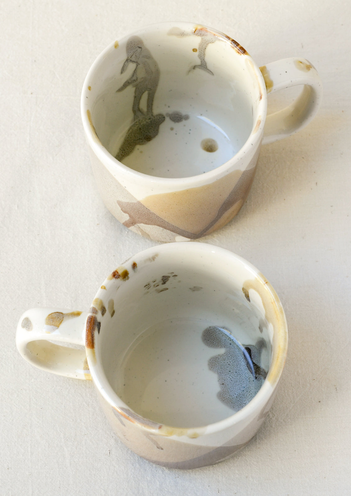 A white ceramic mug with a painted abstract design in brown and grey.