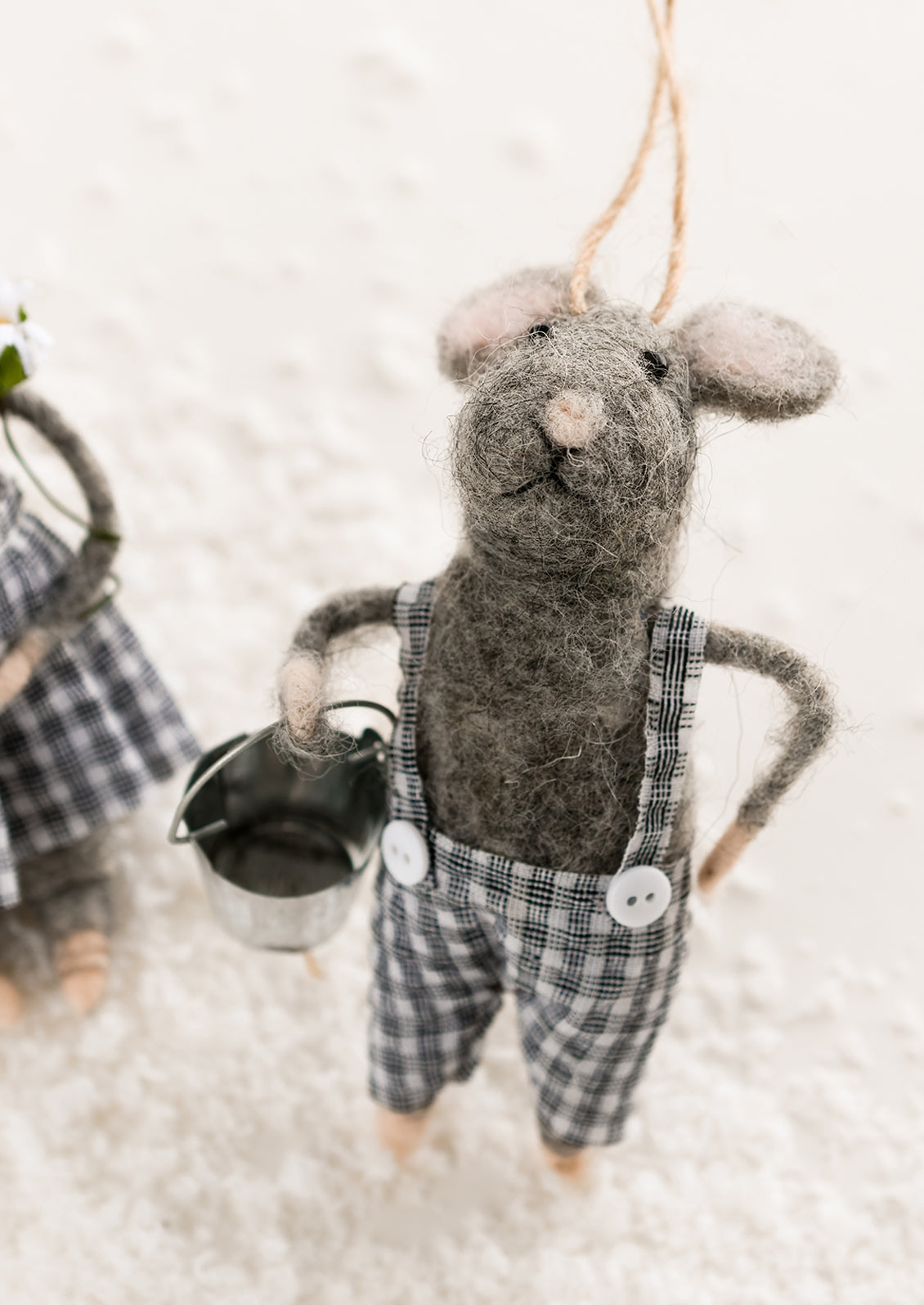 A felted grey mouse ornament in gingham suspenders, holding metal bucket.