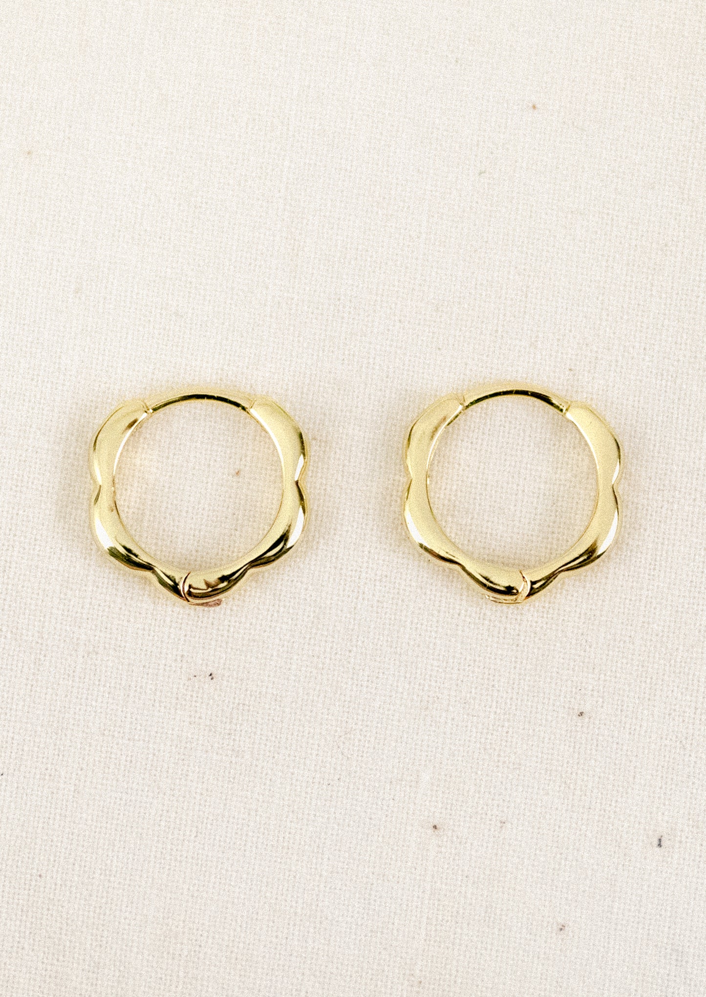 A pair of small gold hoop earrings with a scallop edge design