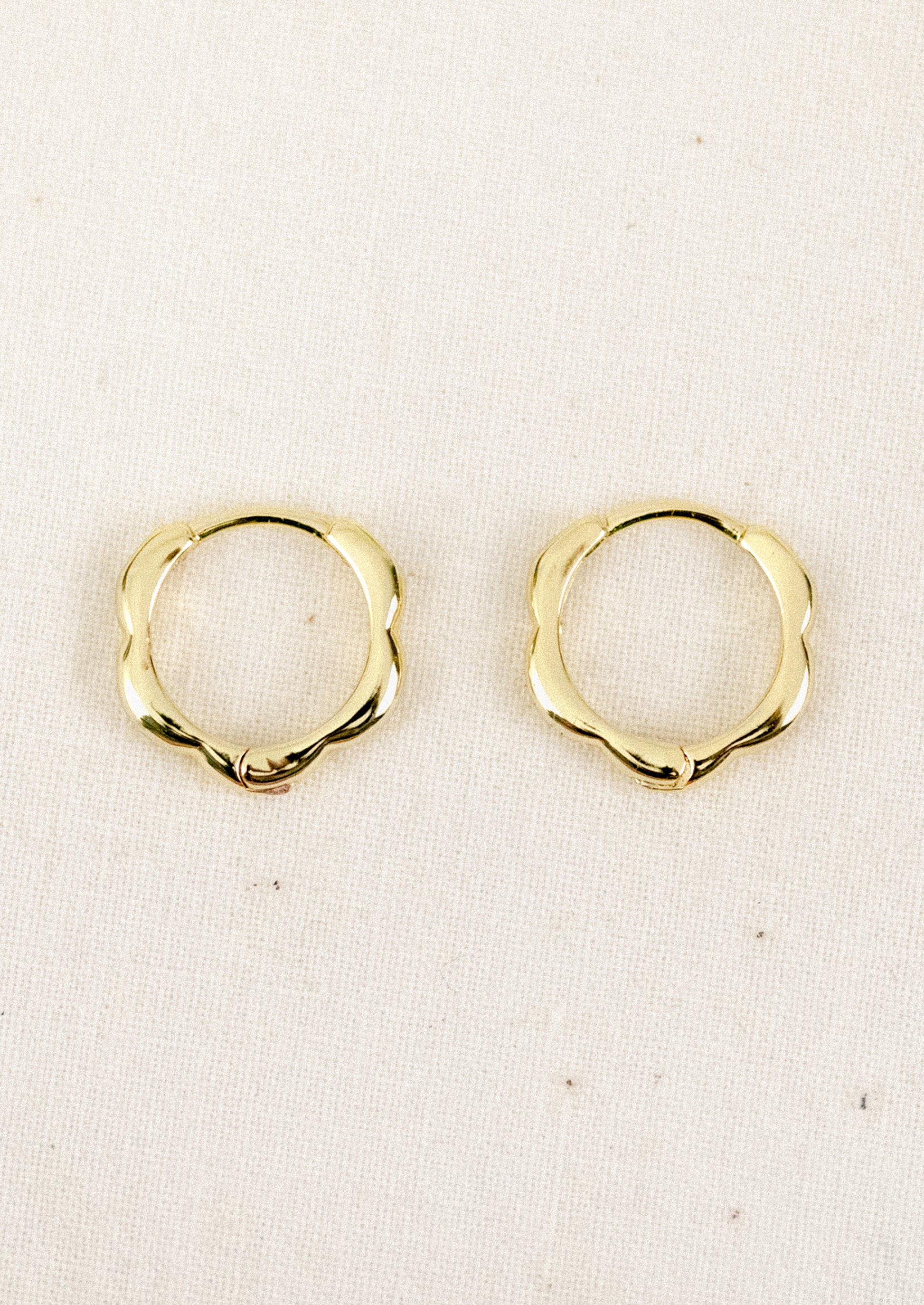 A pair of small gold hoop earrings with a scallop edge design