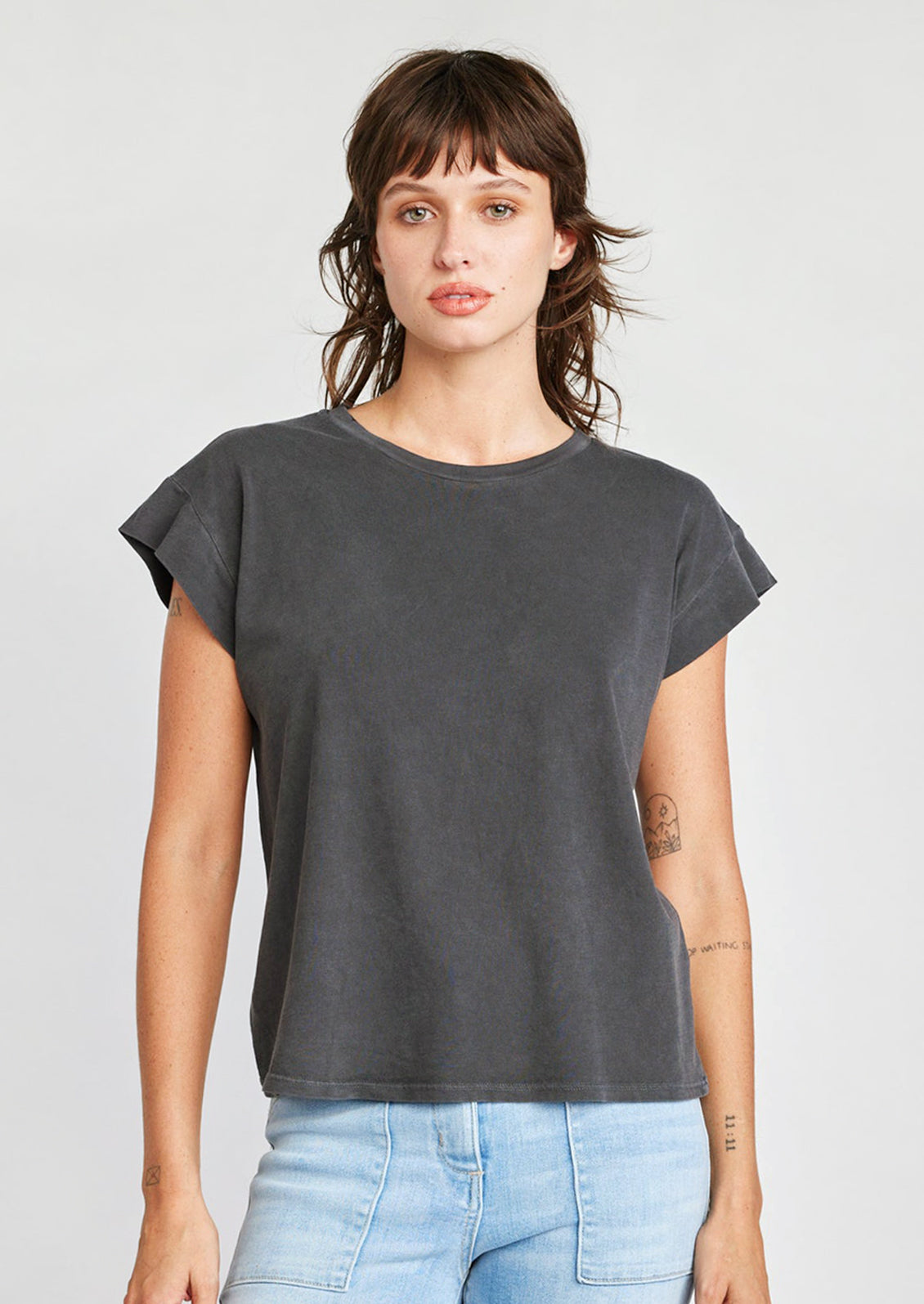 A woman wearing a cap sleeve muscle tee in charcoal color.