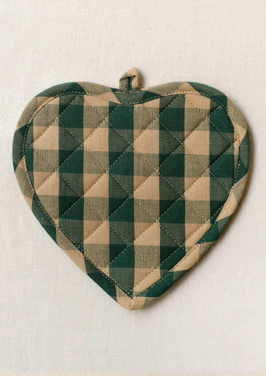 A heart shaped pot holder with a green and tan gingham pattern.