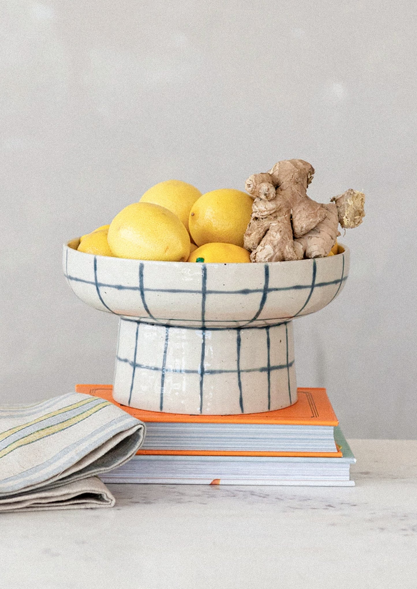 A footed pedestal bowl in natural ceramic with blue painted grid pattern.