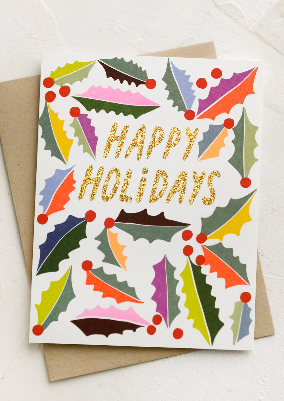 A greeting card with multicolor holly leaf pattern, text reads "Happy holidays".