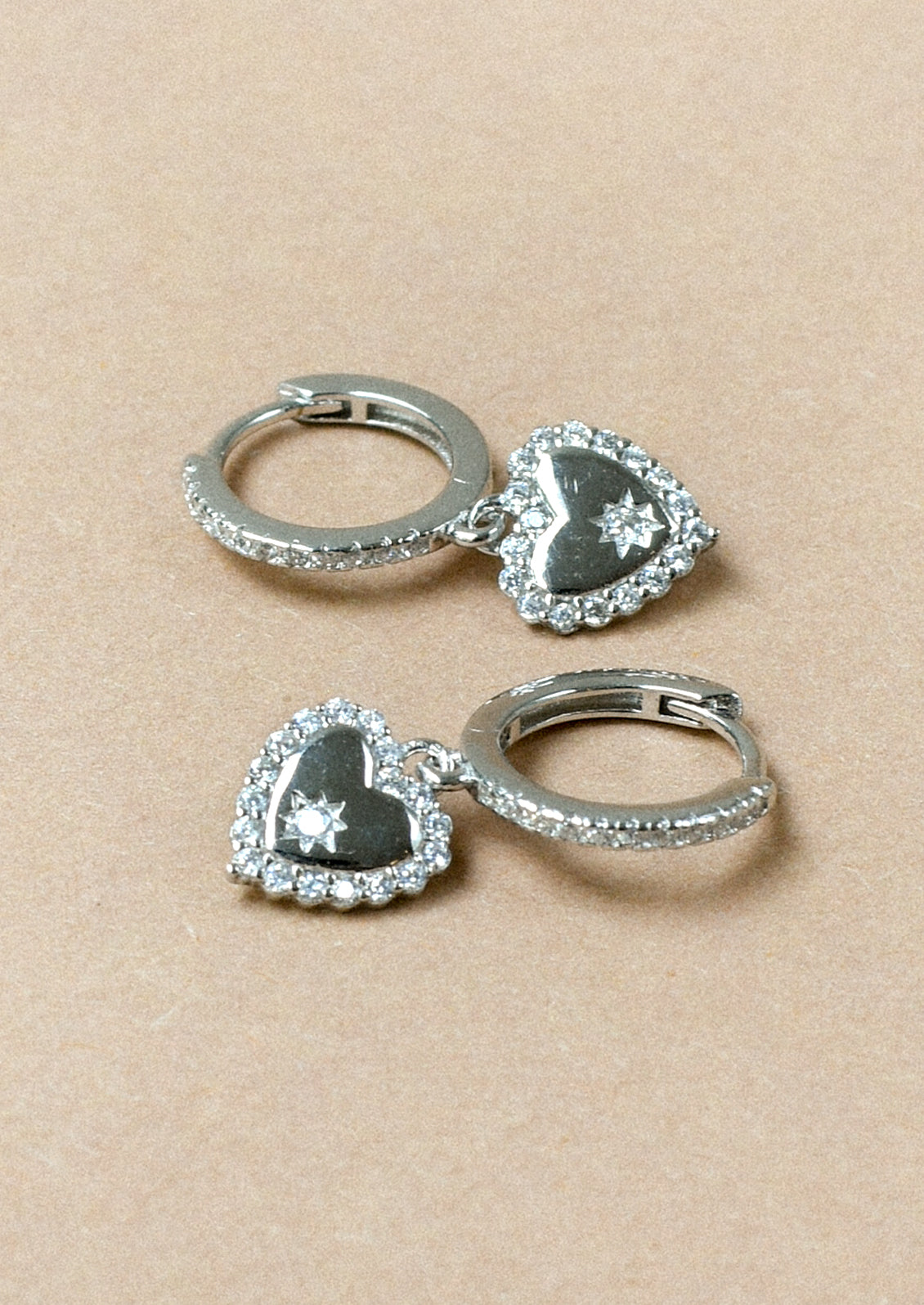A pair of sterling silver huggie hoop earrings with dangling heart charms adorned with cubic zirconia gems.