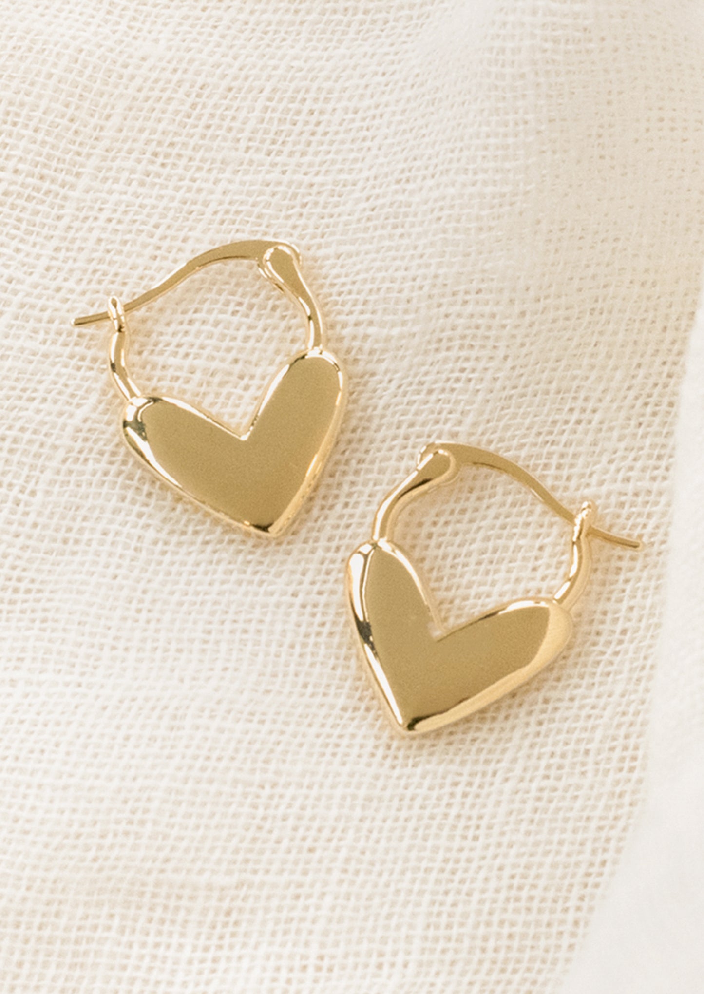 Gold heart-shaped hoop earrings on a light beige background