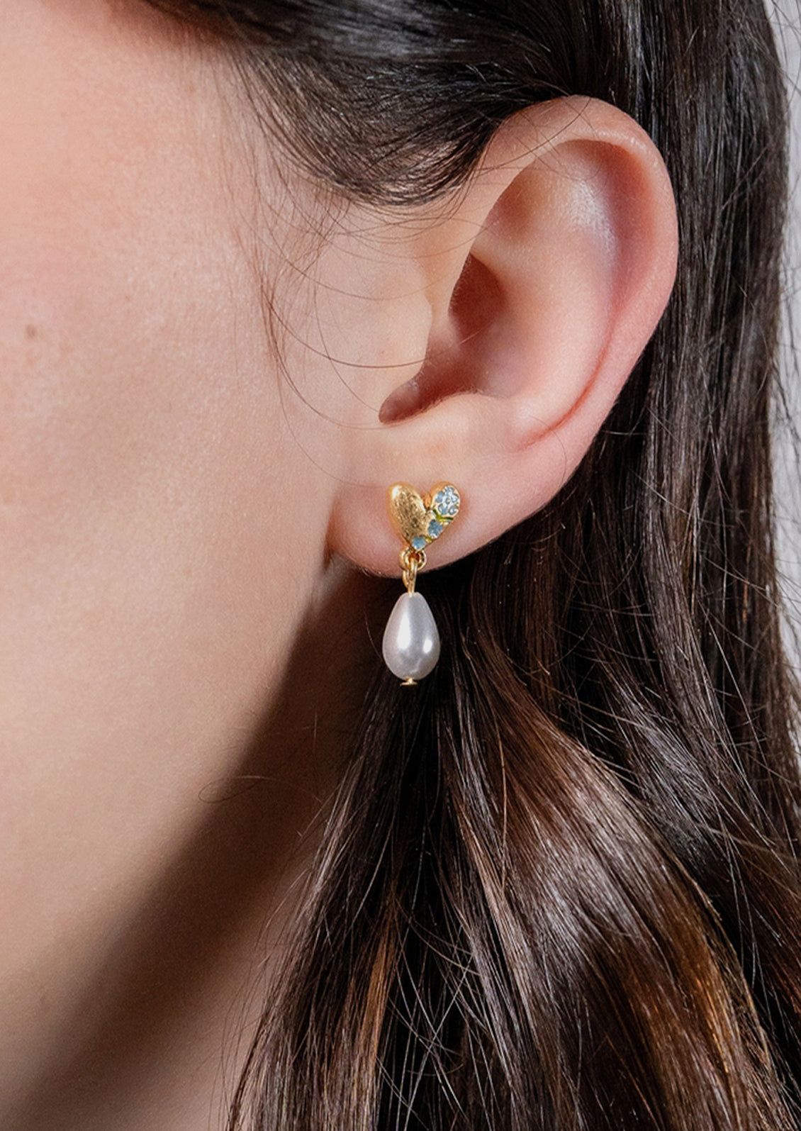 A pair of gold heart shaped earrings with a  dangling pearl.