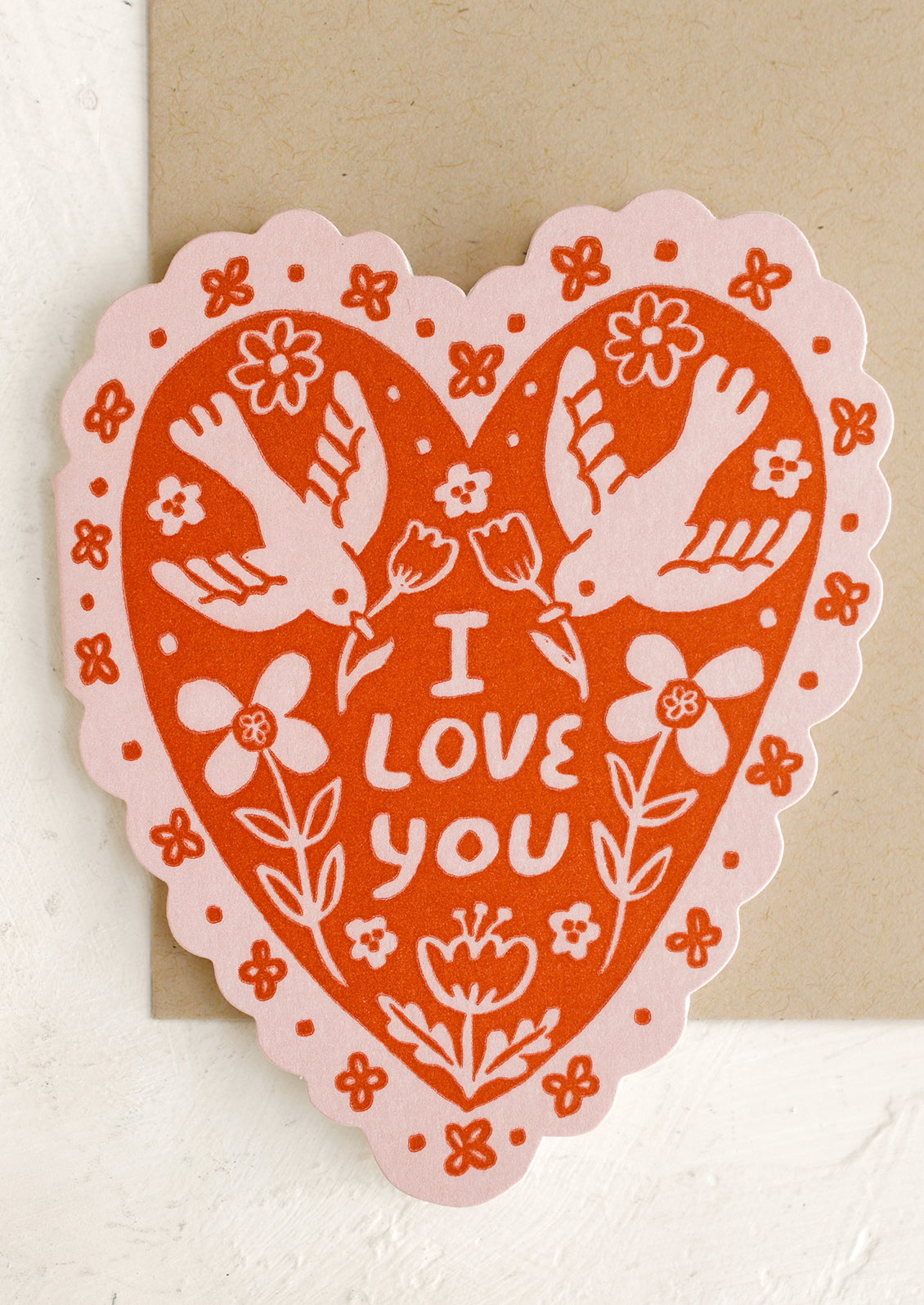 A heart shaped card in pink and red with scalloped edges and doves pattern, text on front reads "I Love You".