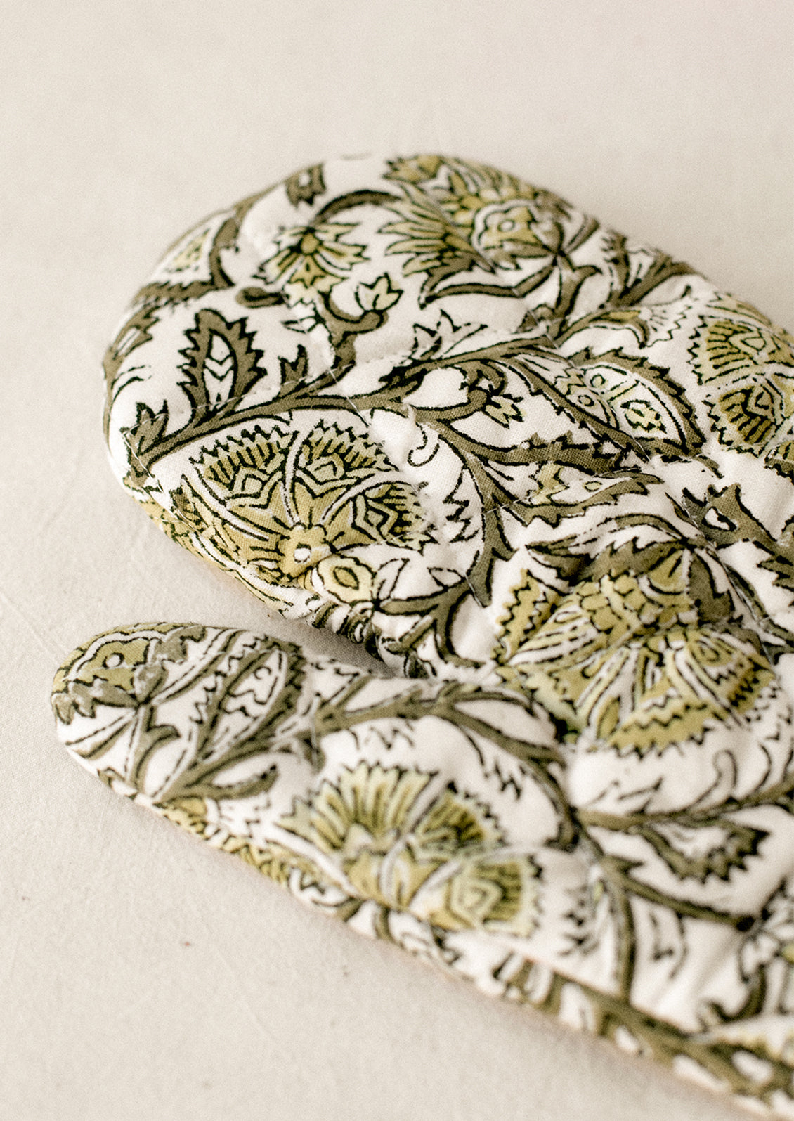 A quilted cotton oven mitt in green floral block print pattern.