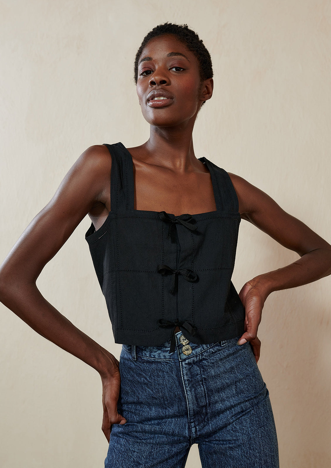 A woman wearing a black square neck tank with tie details at front.