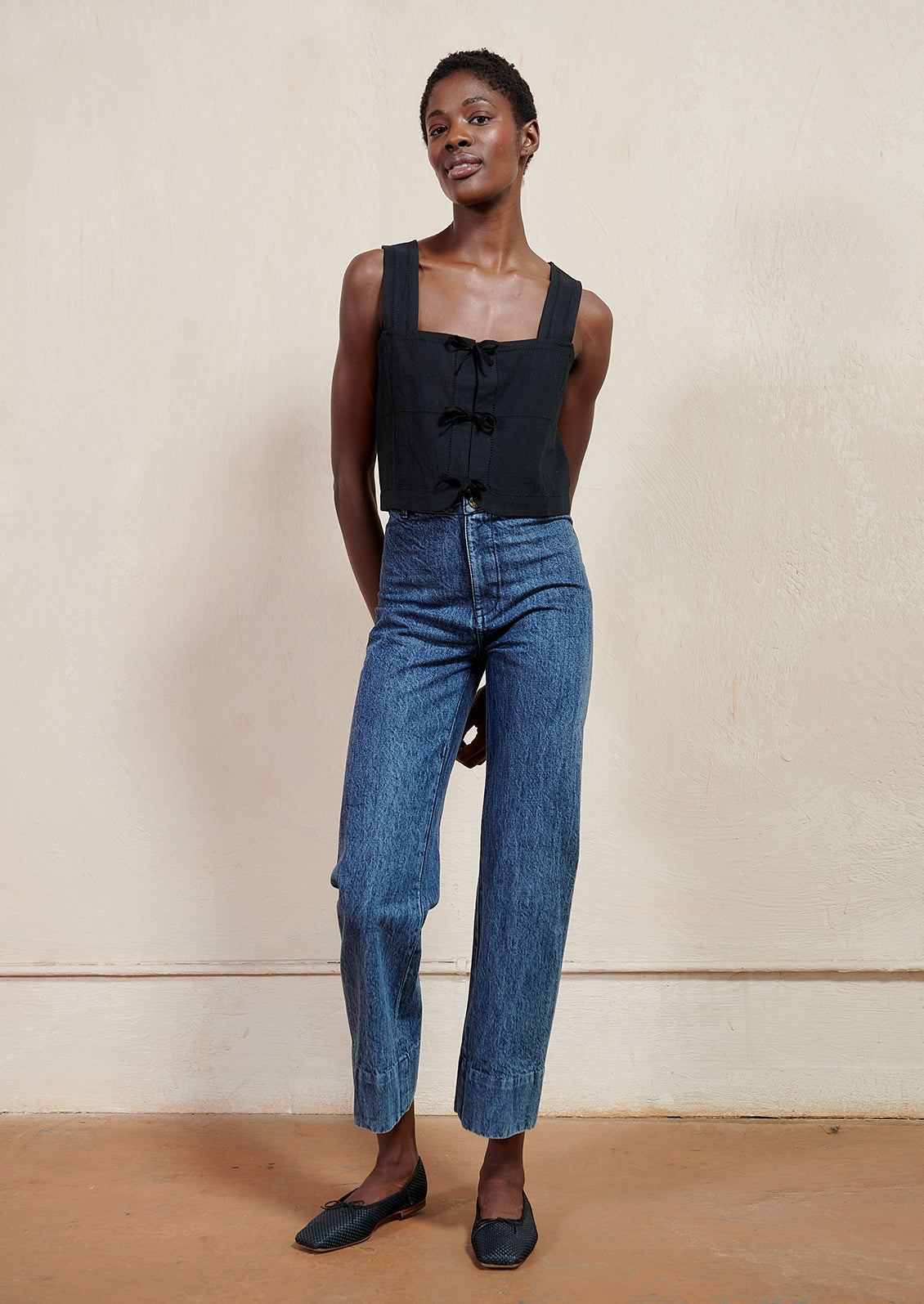 A woman wearing a black square neck tank and blue jeans.