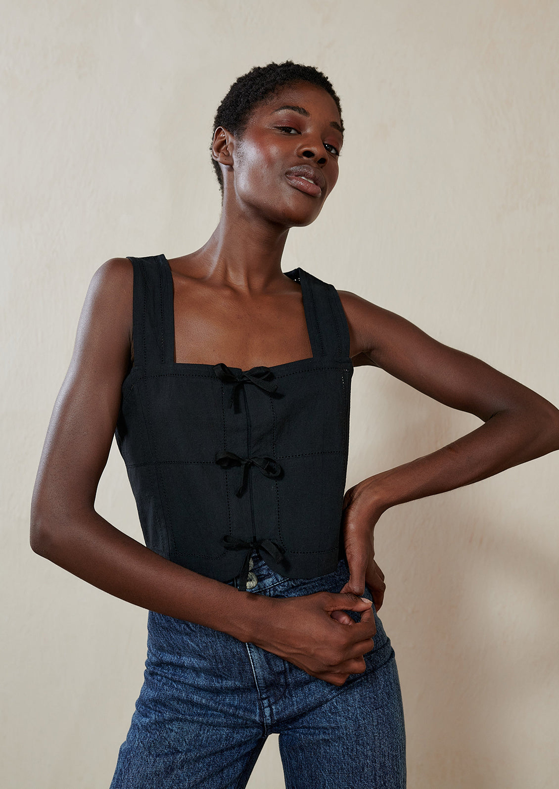 A woman wearing a black square neck tank with tie details at front.