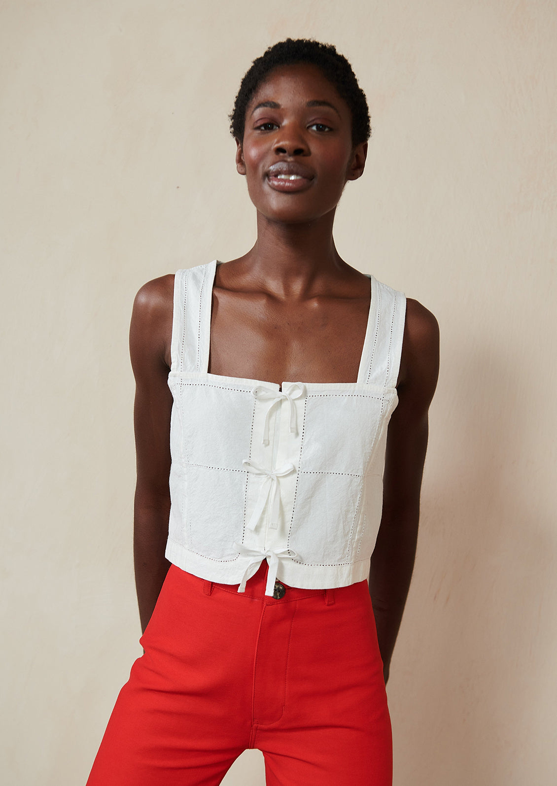 A woman wearing a white square neck tank with ties at front.