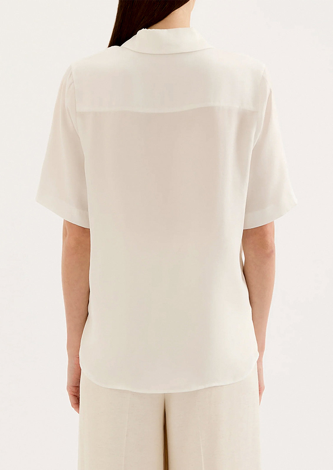 A woman wearing a draped short sleeve button up shirt in white.