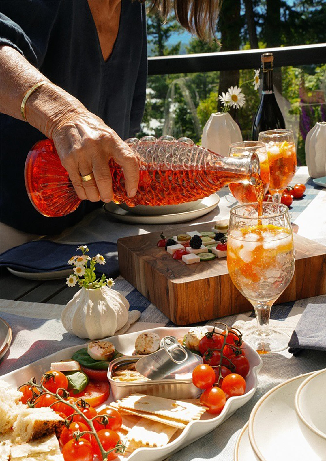 A person pouring orange liquid from fish shaped glass bottle.