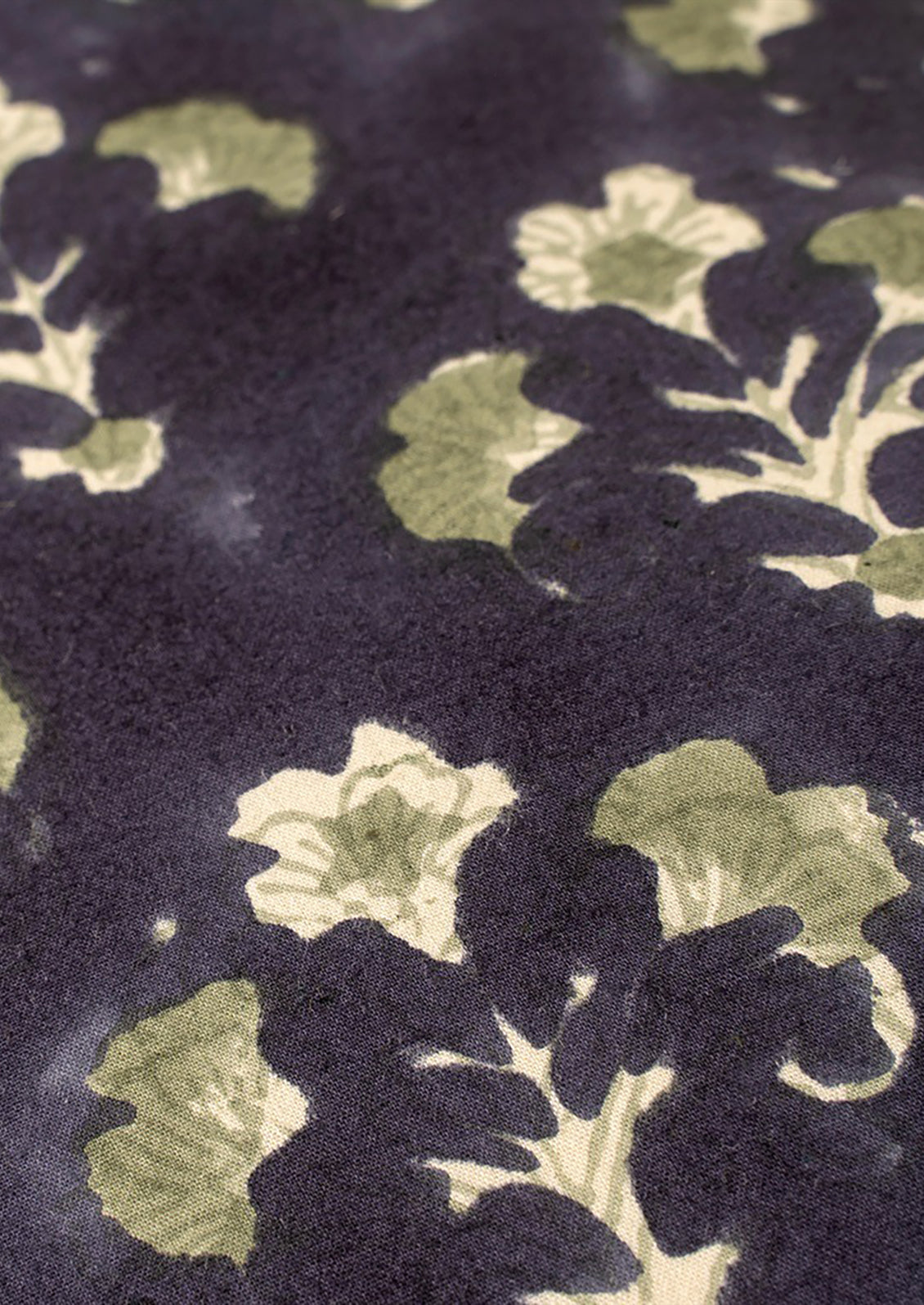 A block printed throw pillow with dark blue background and sage green floral print.
