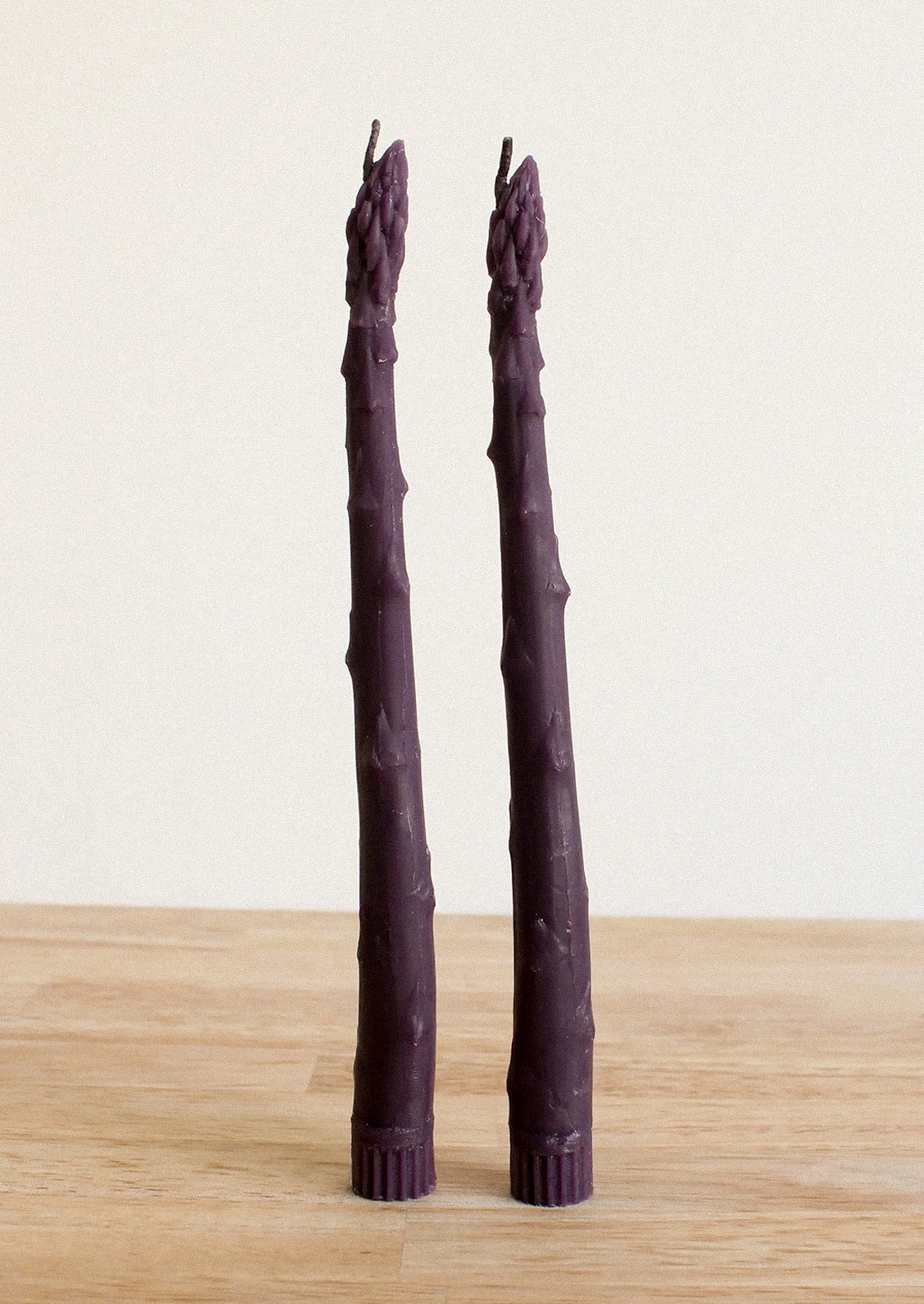 Two purple asparagus shaped taper candles on a white background