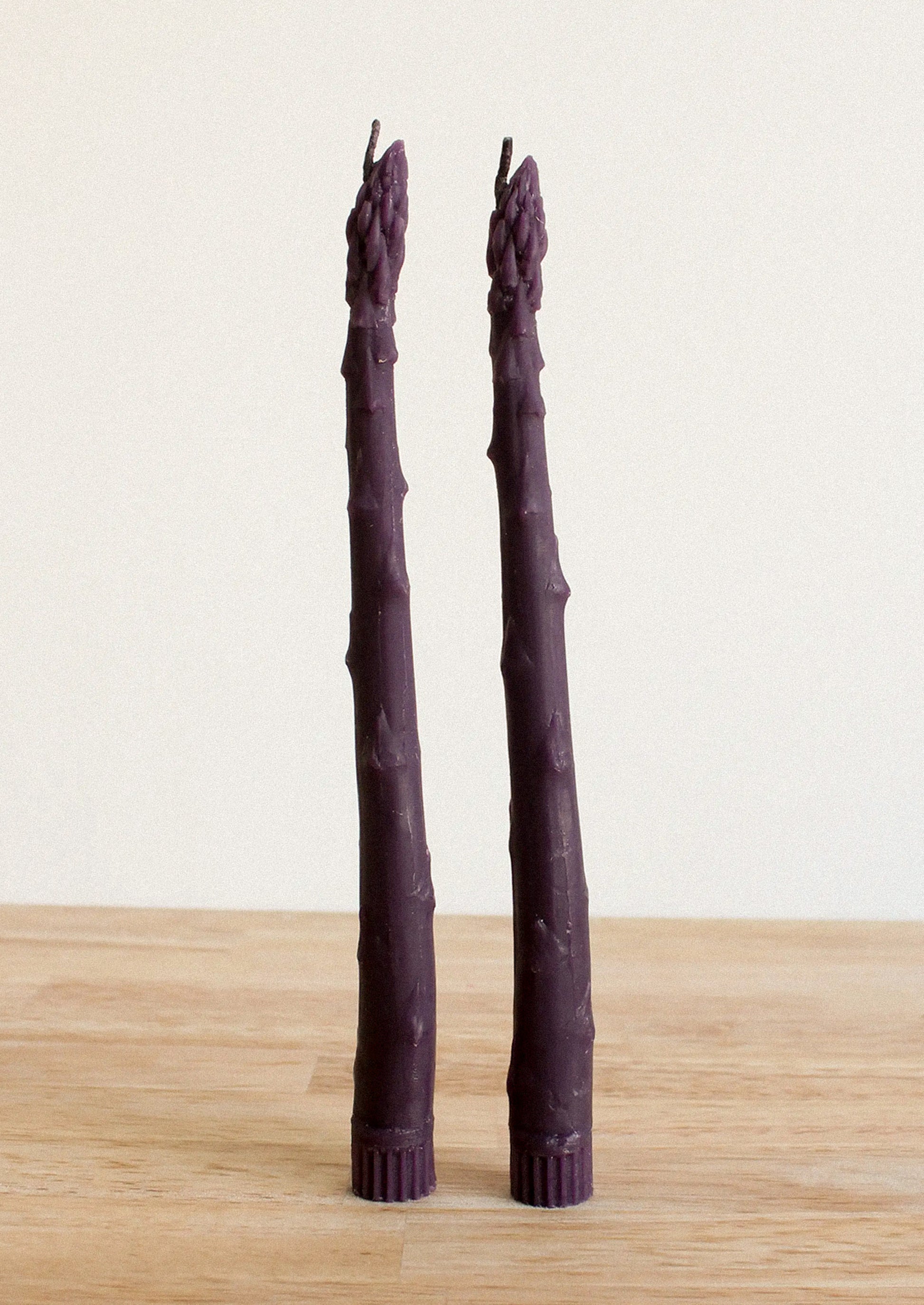 Two purple asparagus shaped taper candles on a white background