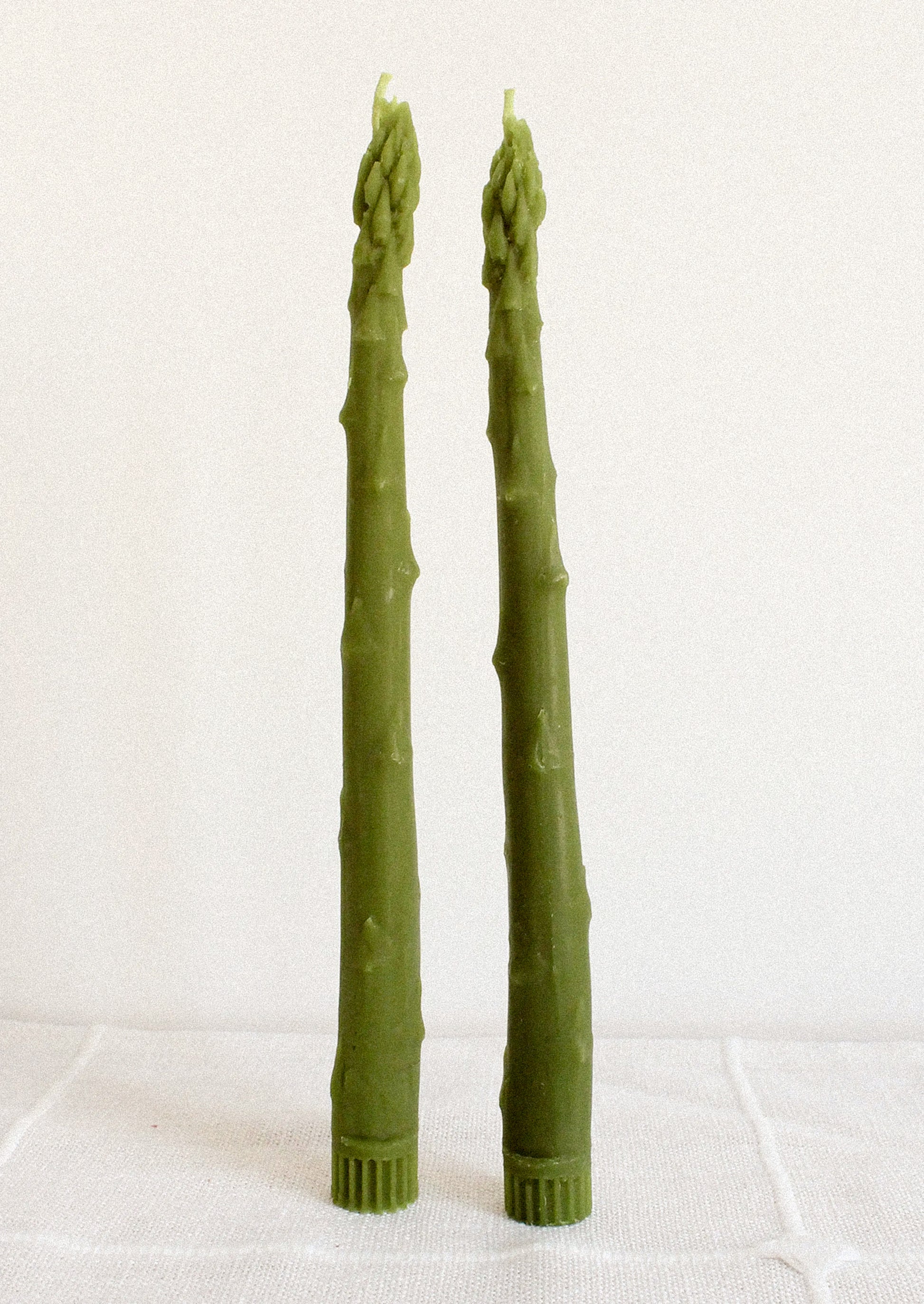 Two green asparagus shaped taper candles on a white background