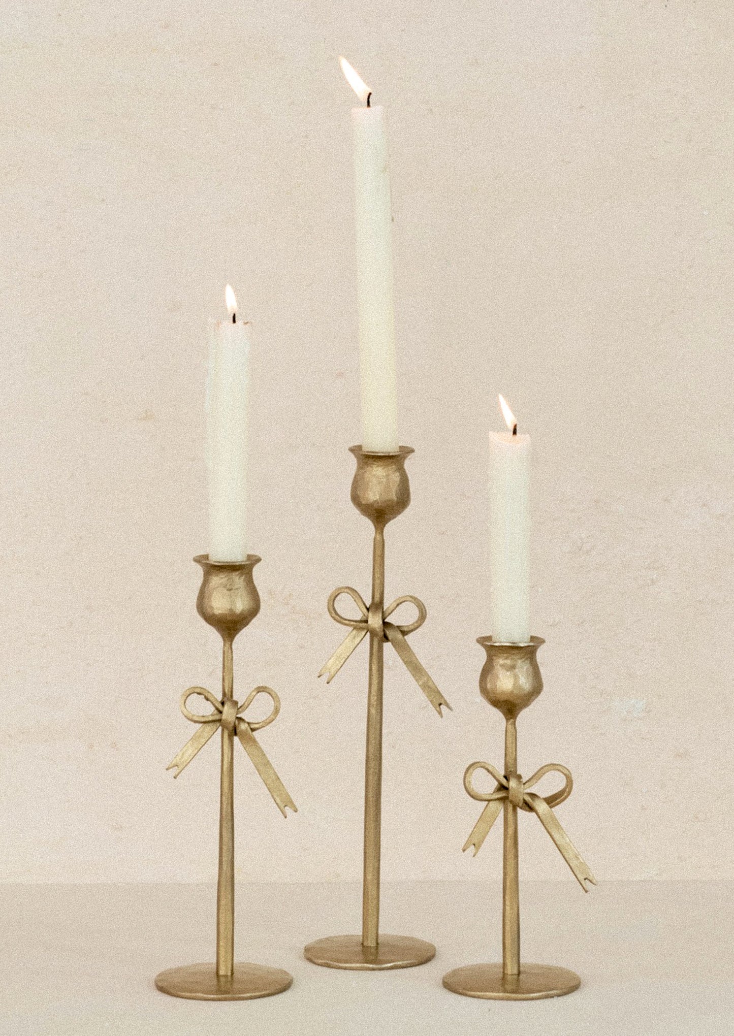 Three gold candle holders with candles on a beige background