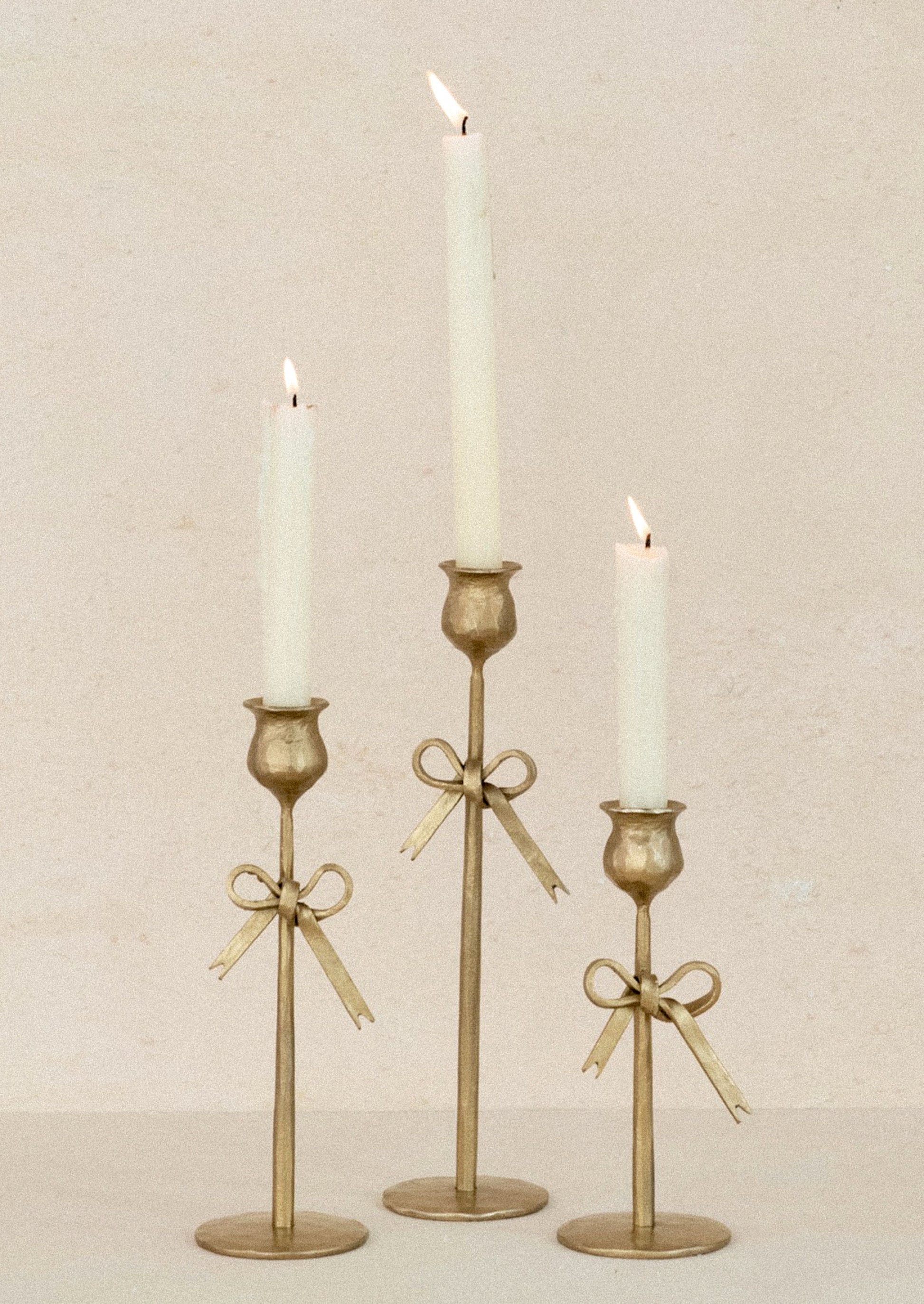 Three gold candle holders with candles on a beige background