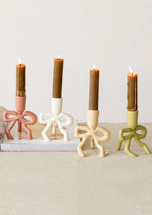 Four bow-shaped candle holders with candles on a neutral background
