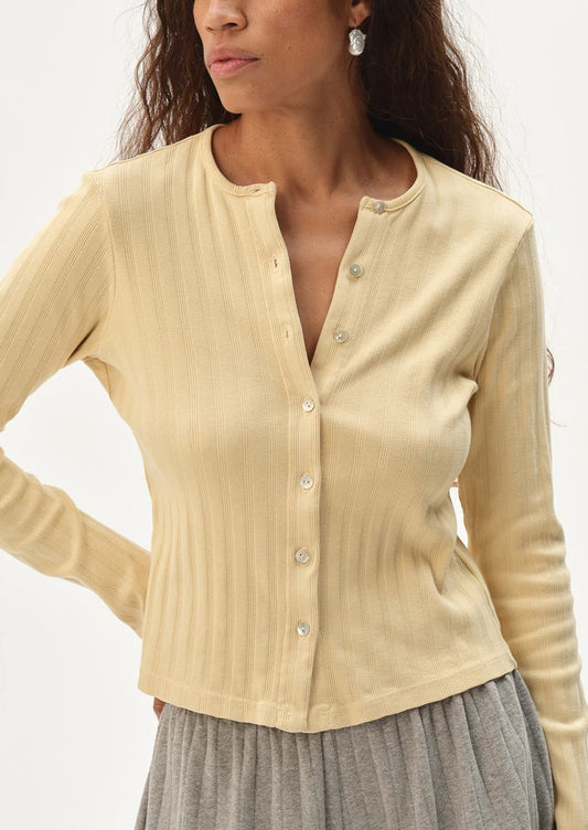 Woman wearing a butter yellow long-sleeve cardigan on a plain background
