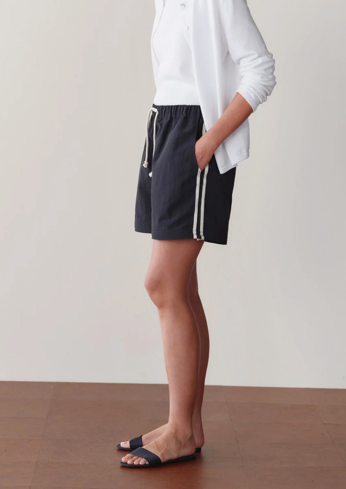 Person wearing black pants with white stripes and a white top against a neutral background