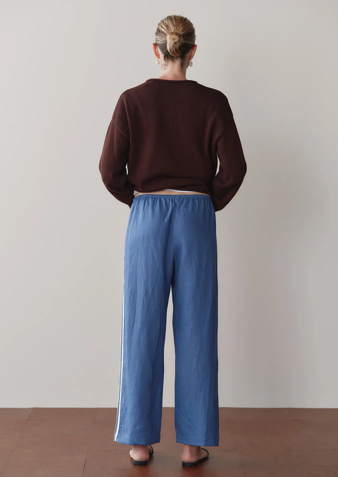 Person wearing a brown sweater and blue pants standing against a plain wall.