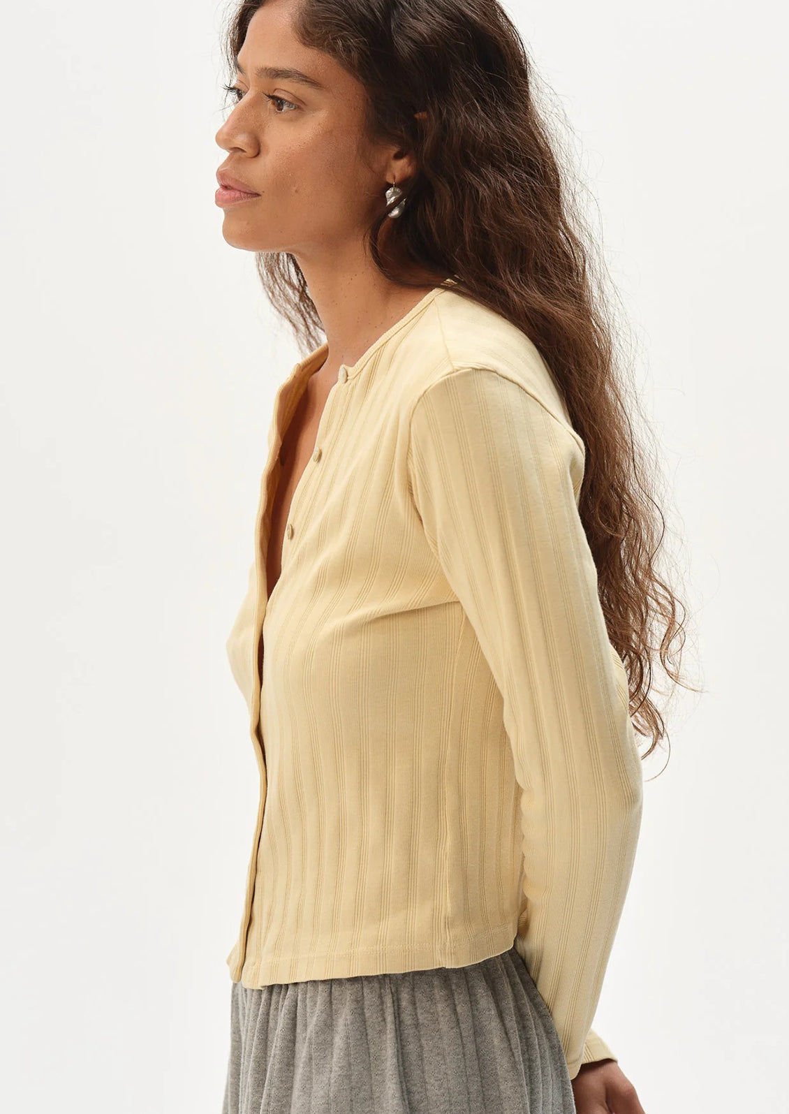 Woman wearing a butter yellow long-sleeve cardigan on a plain background