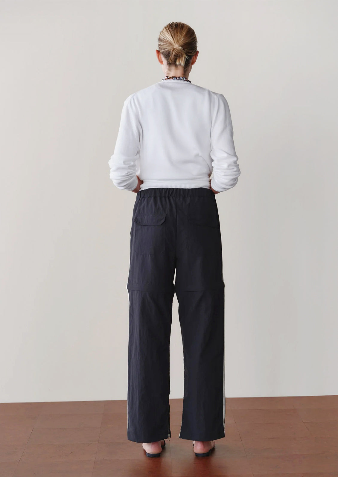 Person wearing black pants with white stripes and a white top against a neutral background