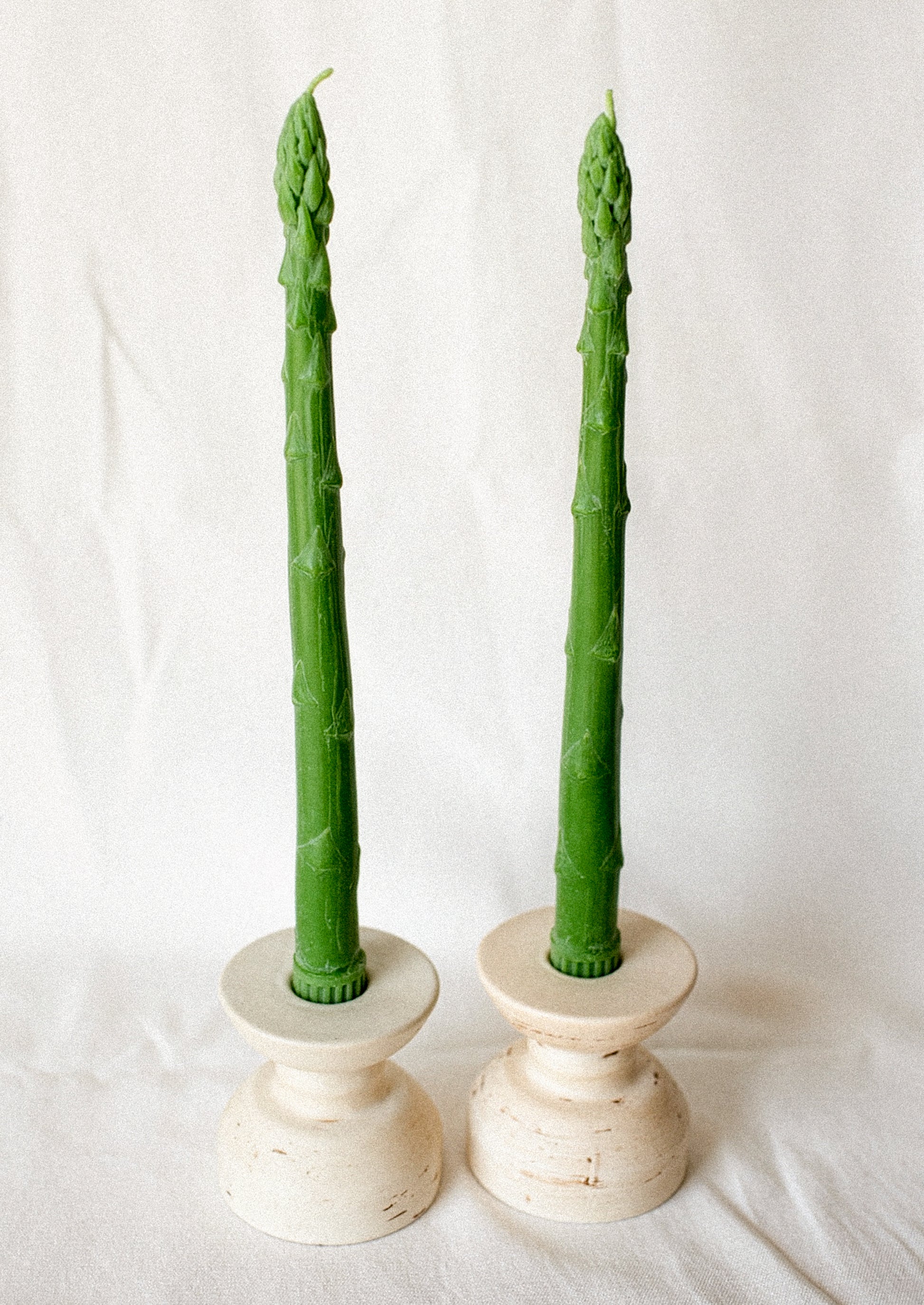 Two green asparagus shaped taper candles on a white background