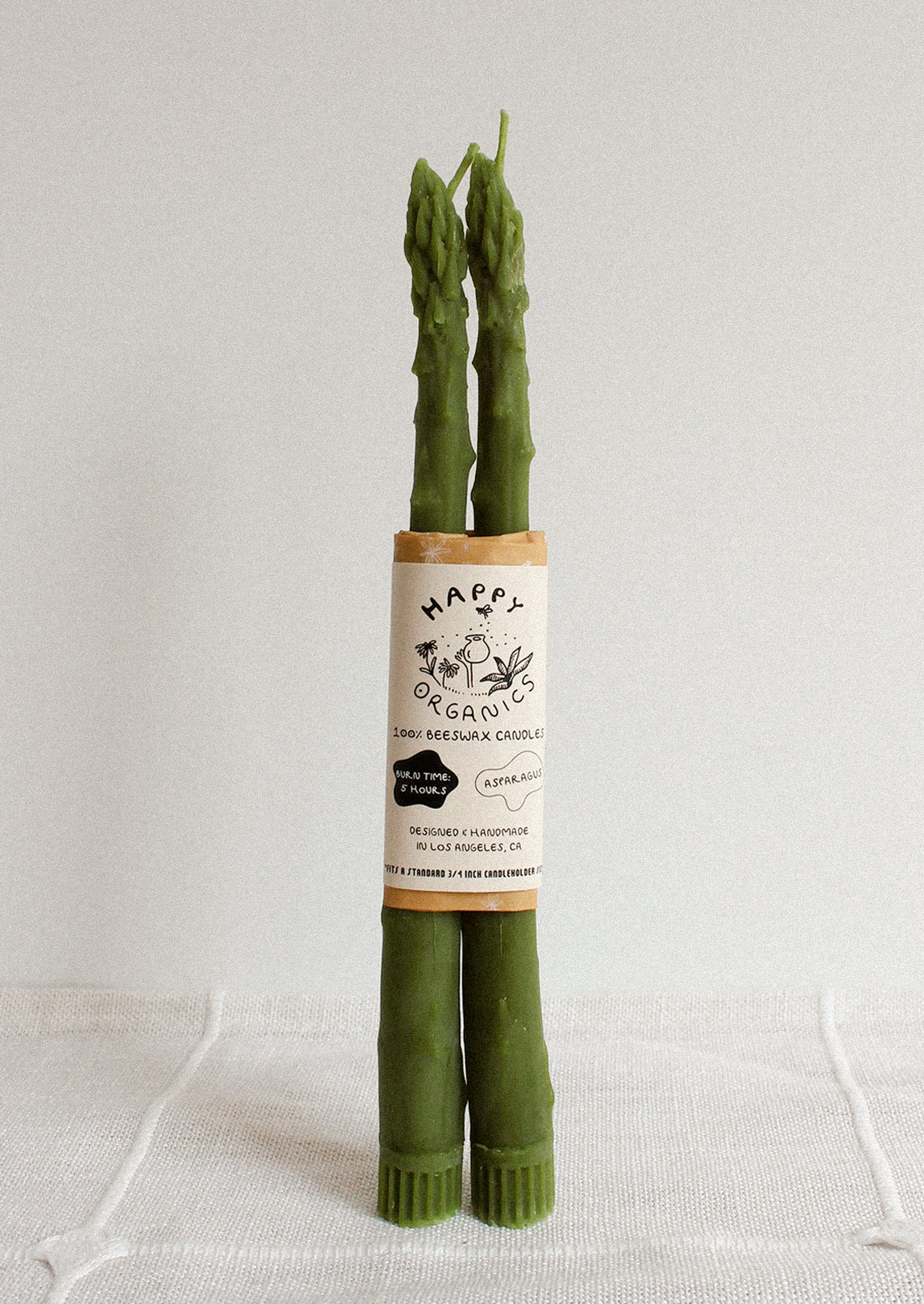 Two green asparagus shaped taper candles on a white background