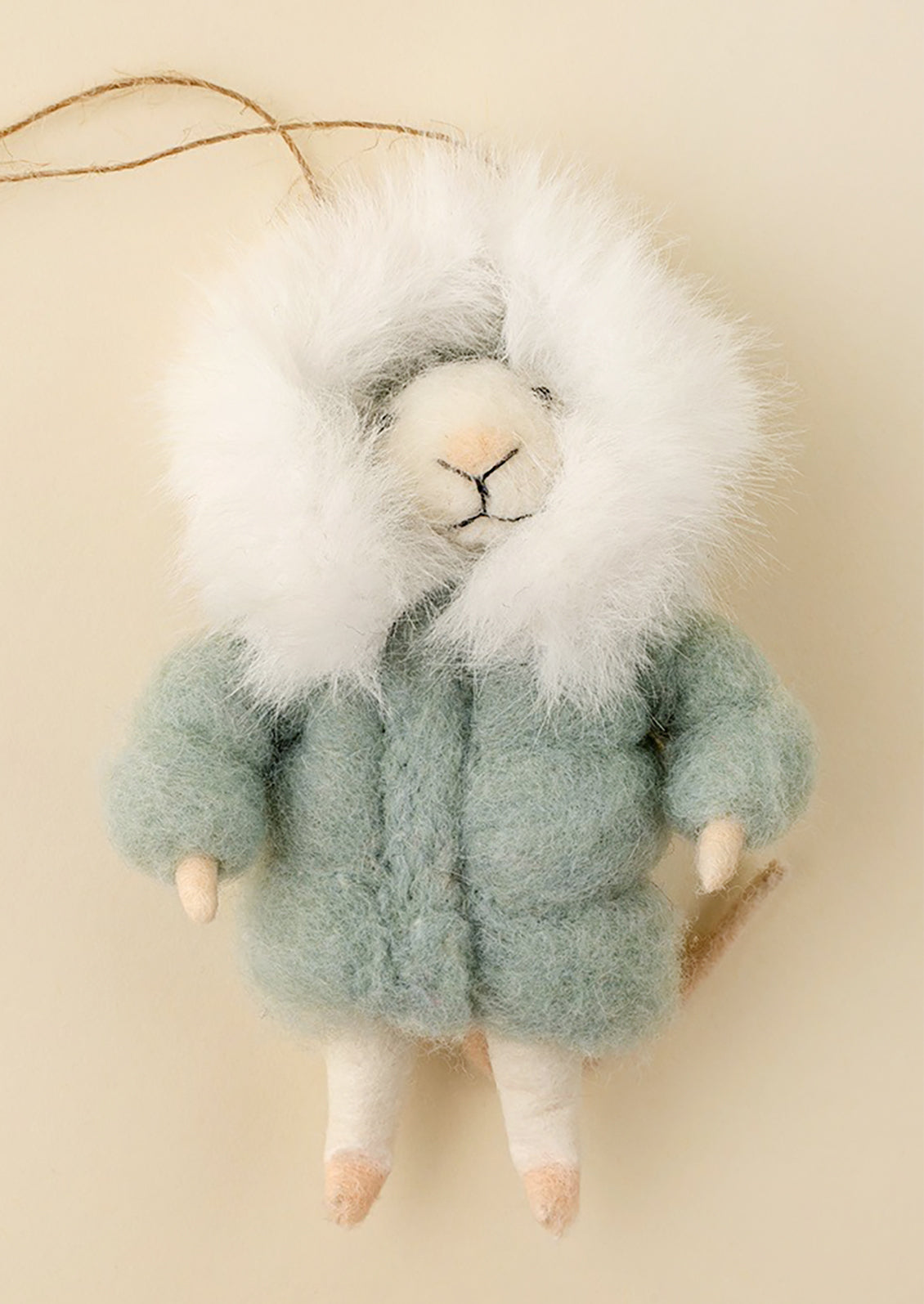 A felted mouse ornament wearing a fuzzy pale green coat and a large white faux-fur hood, hanging against a warm cream background.