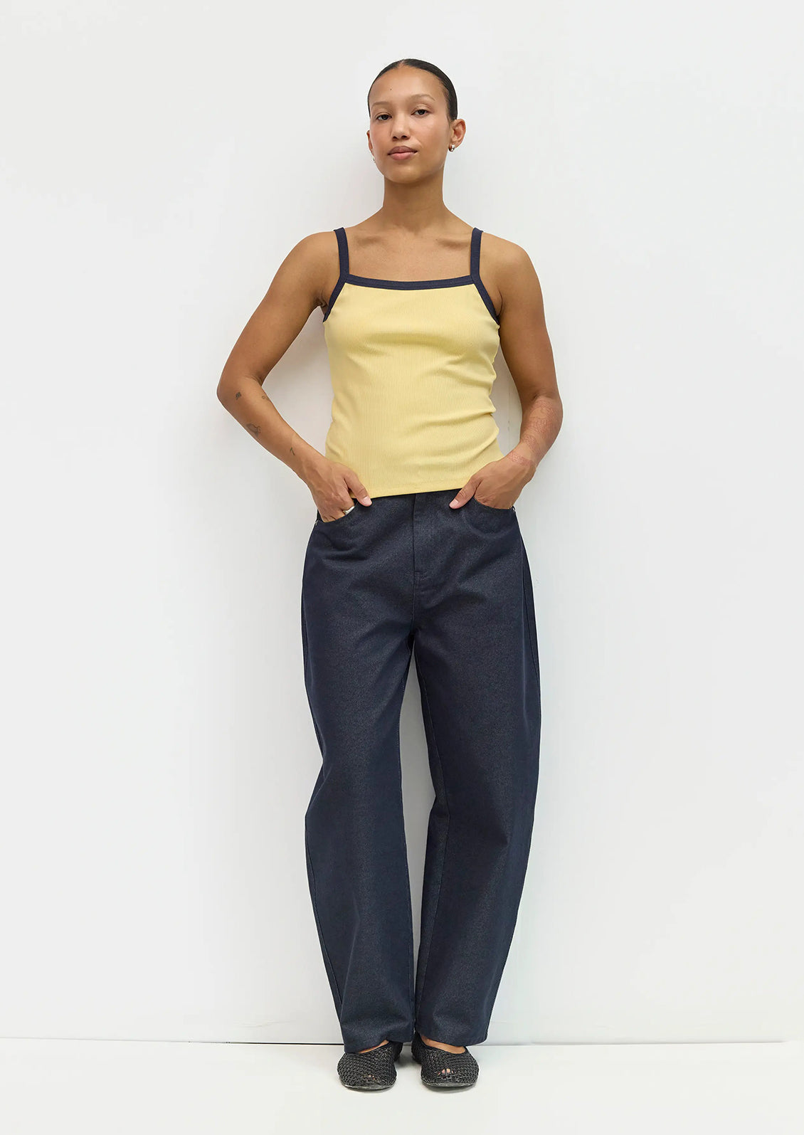 Person wearing a yellow tank top and navy pants against a white background