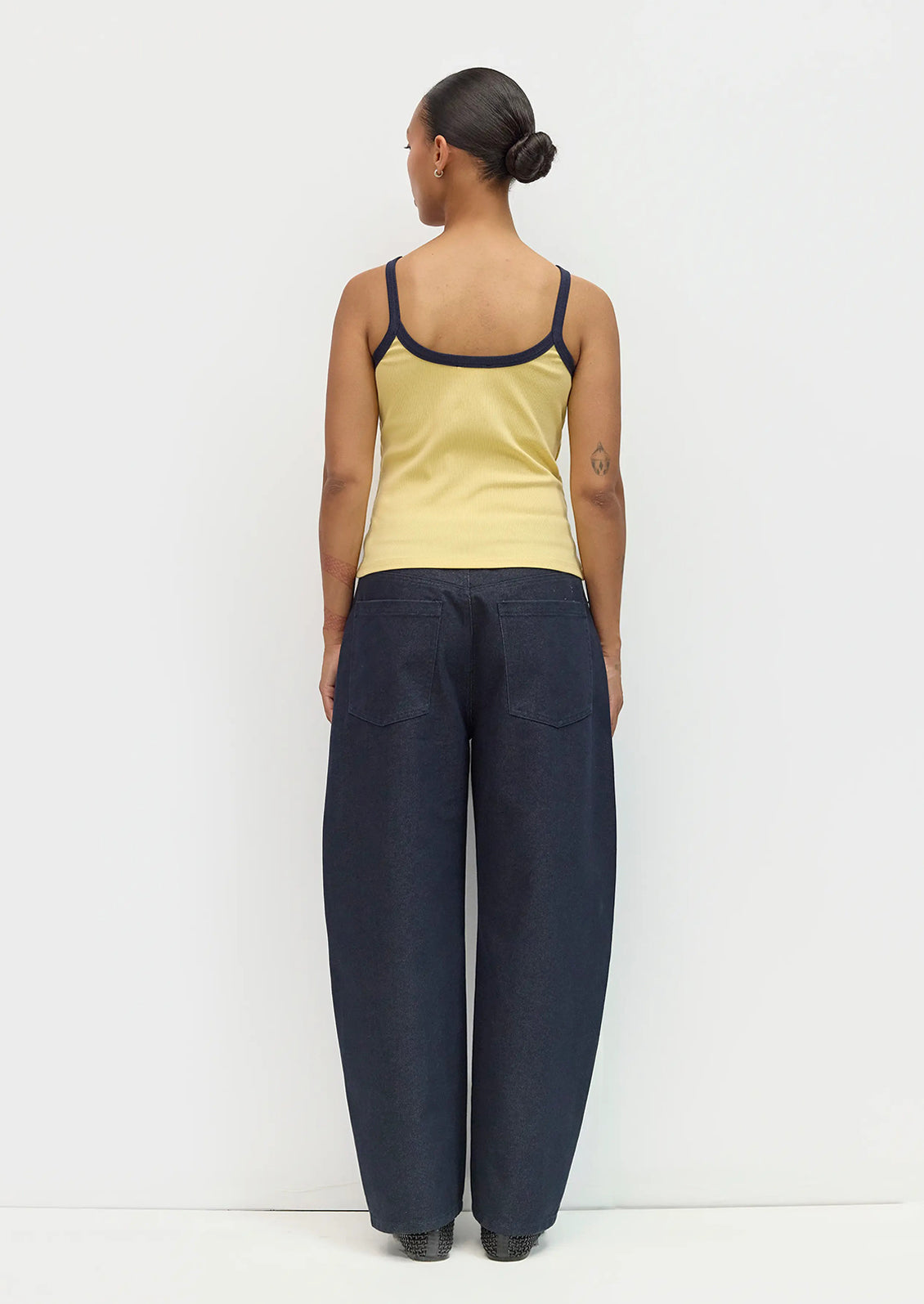Person wearing a yellow tank top and dark blue pants on a white background