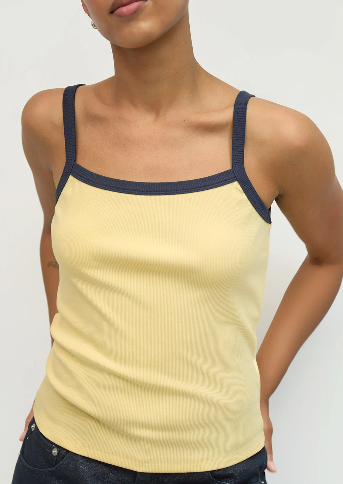 Woman wearing a yellow tank top with navy straps on a plain background