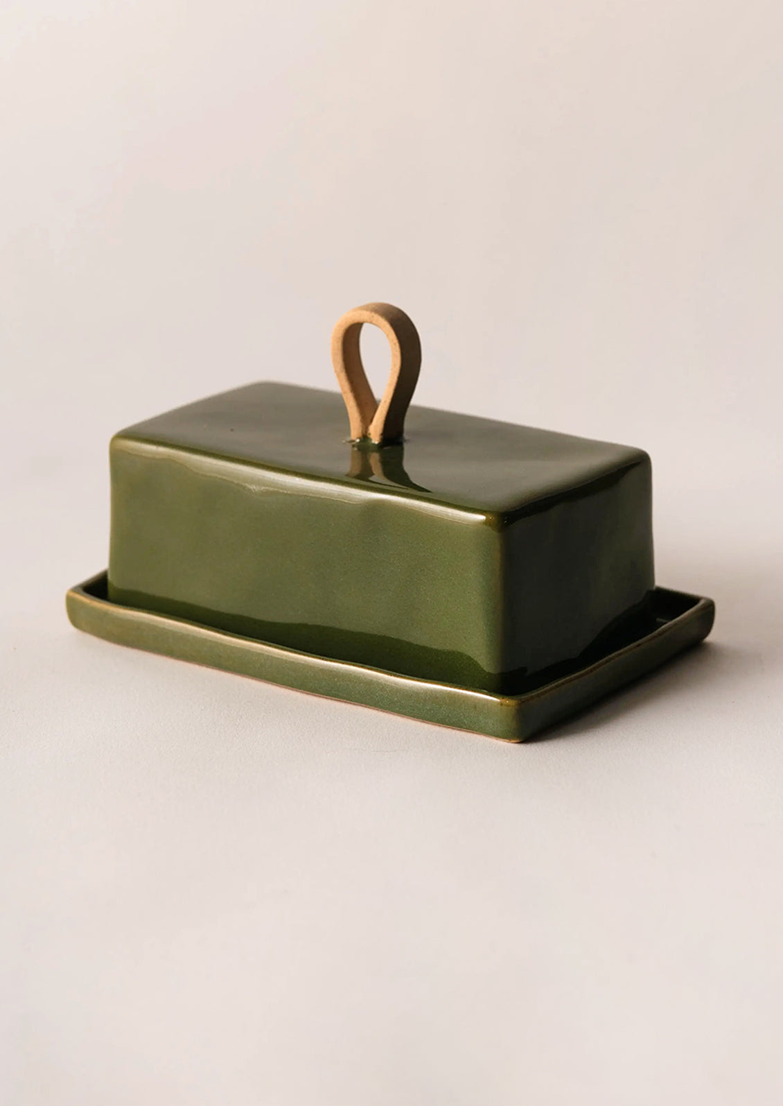 Green ceramic butter dish with wooden handle on a beige background