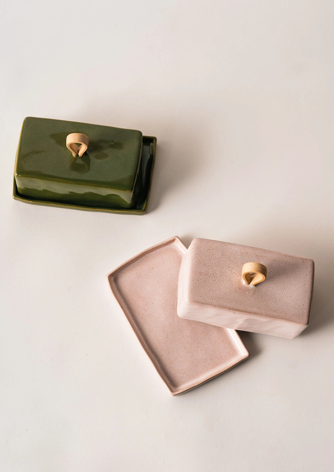 Two ceramic butter dishes, one green and one pink, with tan knobs on a light background.
