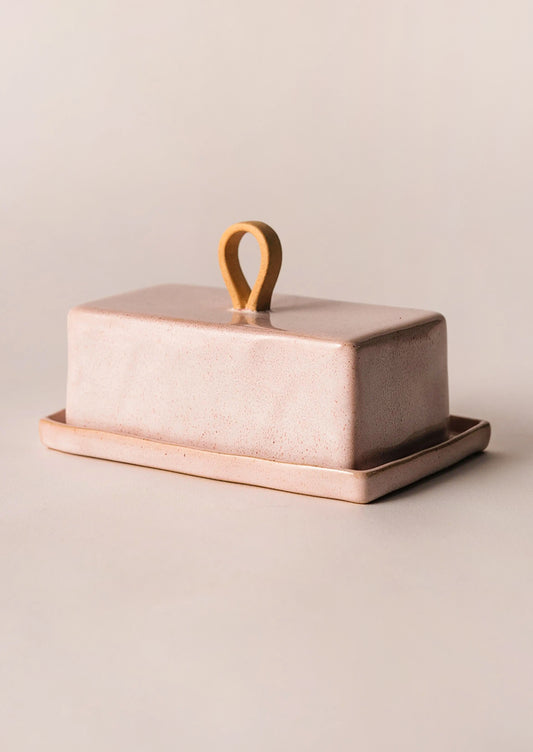 Ceramic butter dish with a lid and handle on a beige background