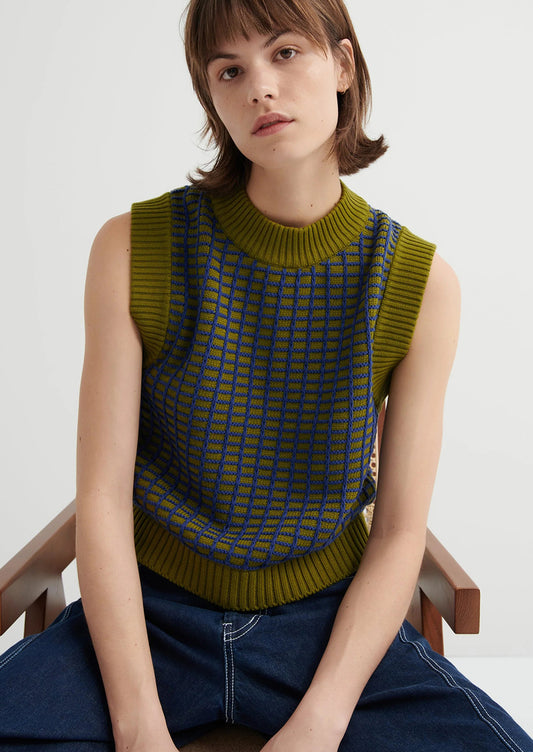 Woman wearing a green patterned sleeveless sweater sitting on a chair.