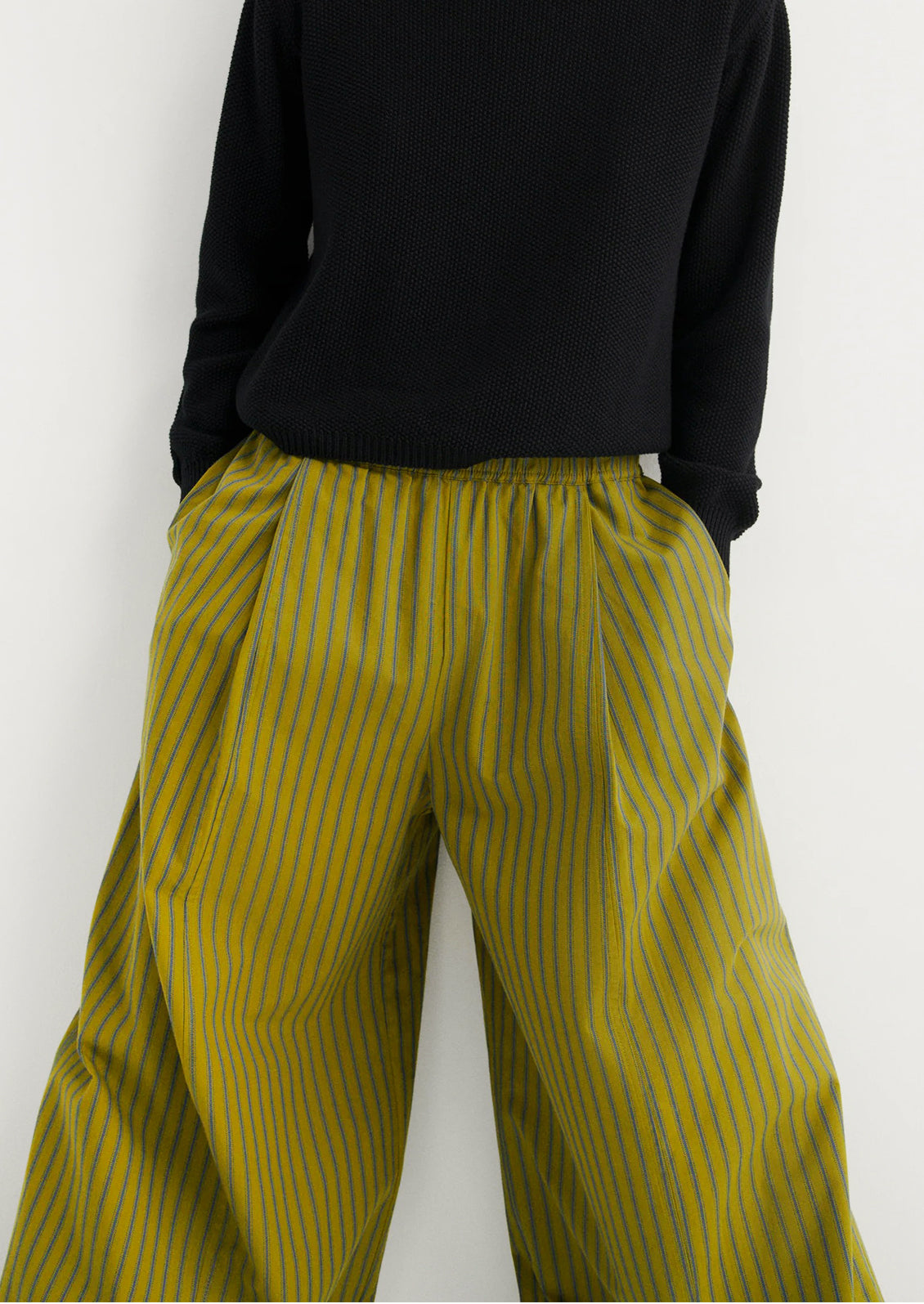 Person wearing black top and yellow striped pants on a white background