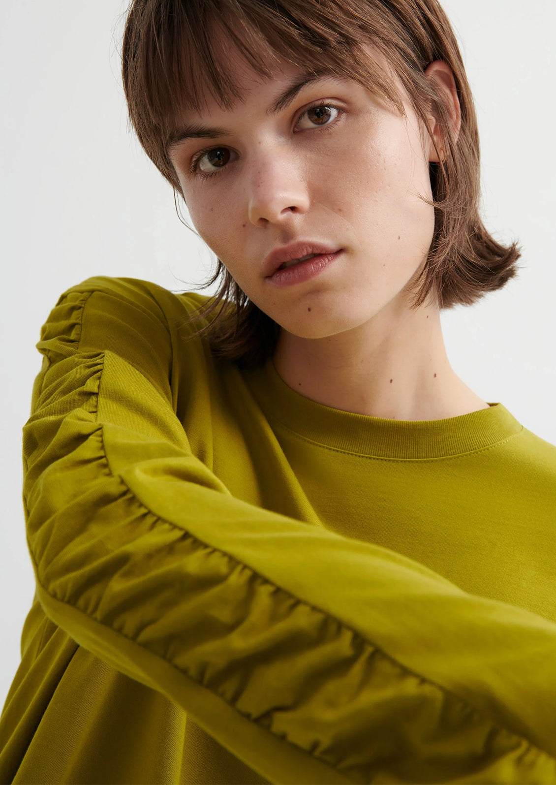 Person wearing a chartreuse long-sleeve shirt with a textured sleeve design on a white background