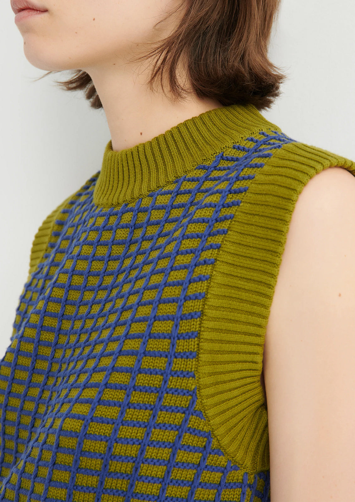Green sleeveless knitted top with blue geometric pattern on a white background
